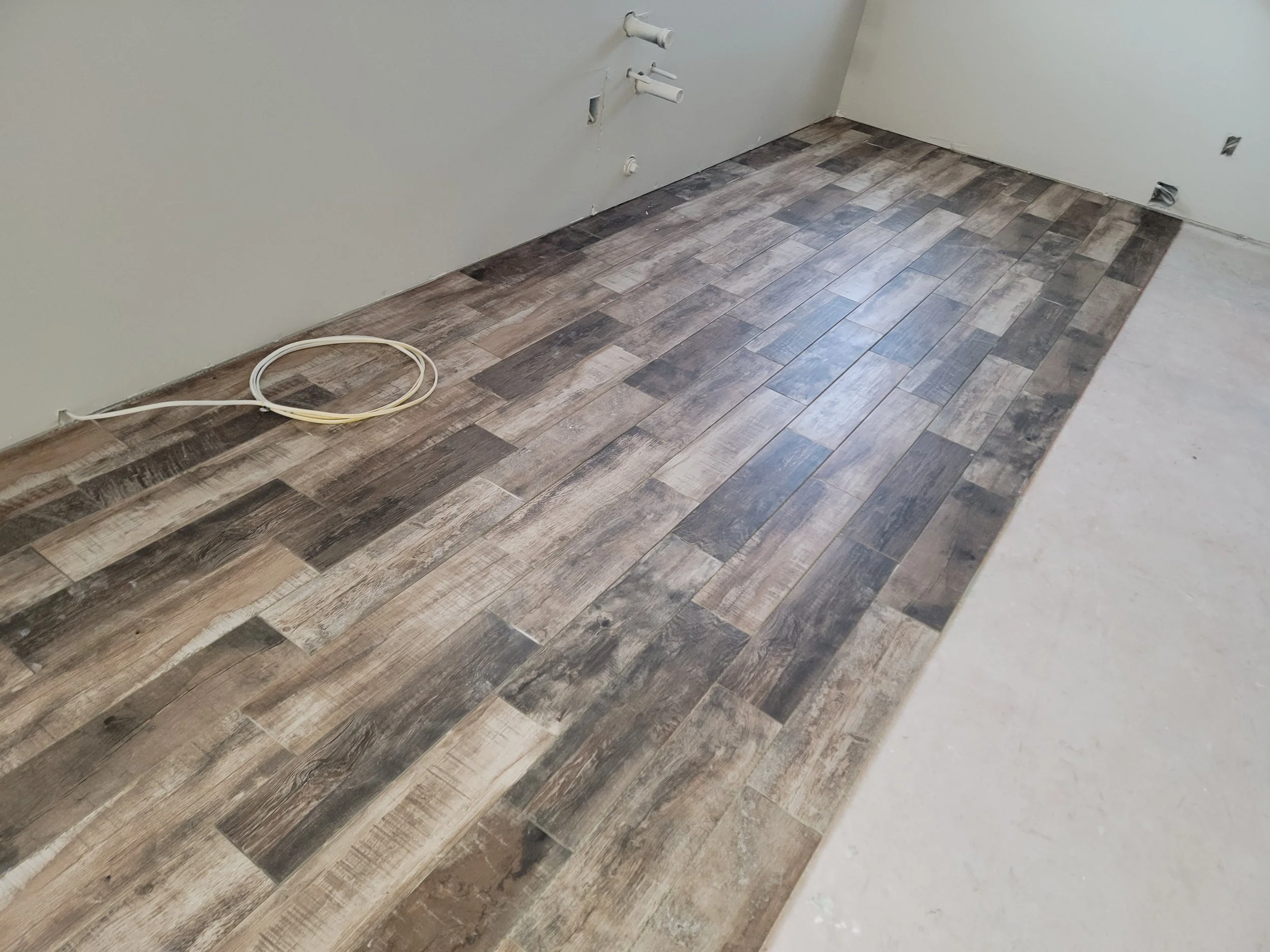 A room under renovation with laminate wood flooring partially installed, some wall outlets exposed, and exposed pipes on the wall.
