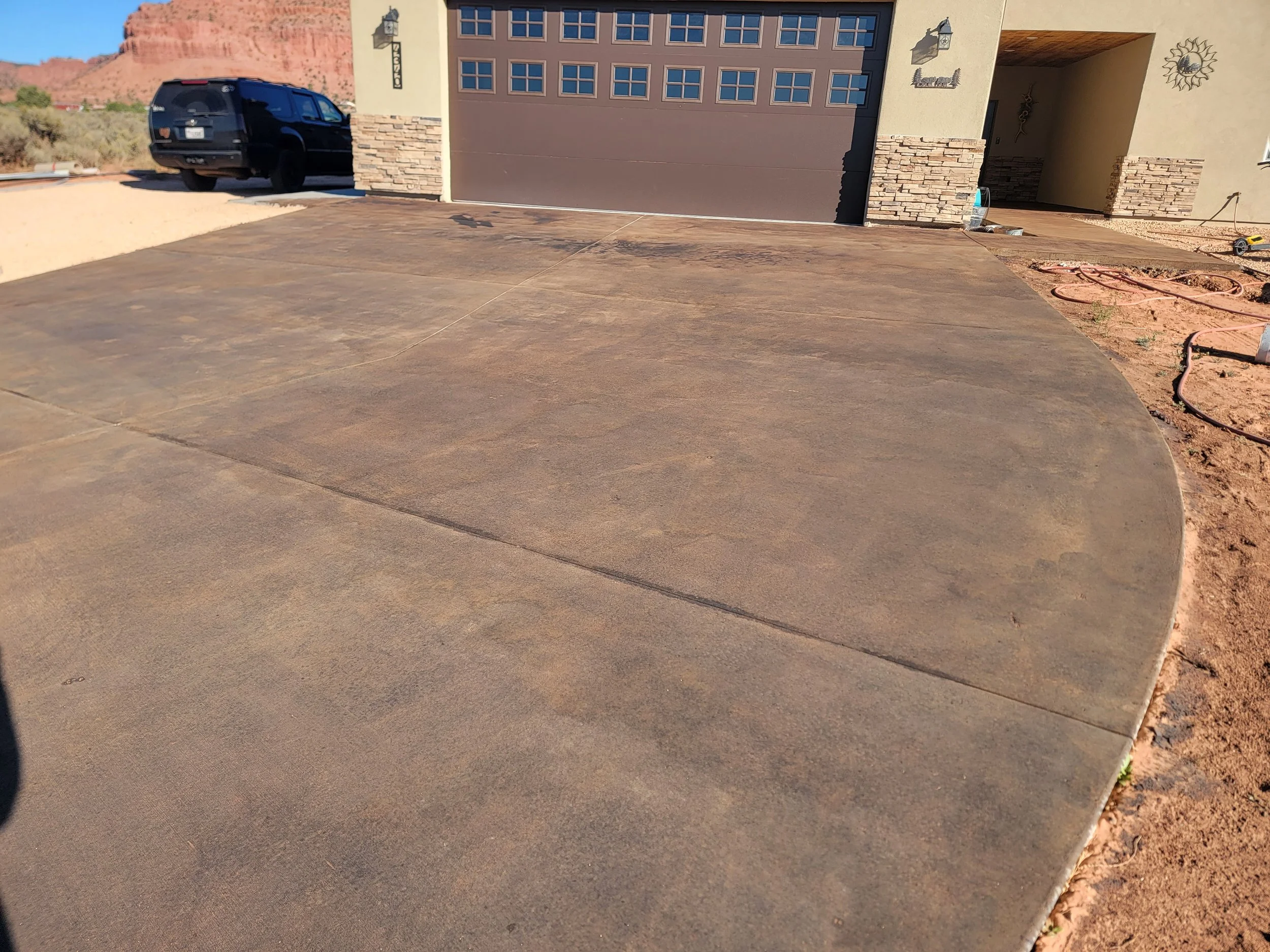 A newly paved concrete driveway in front of a house with a garage door, with landscaping and mountains in the background.