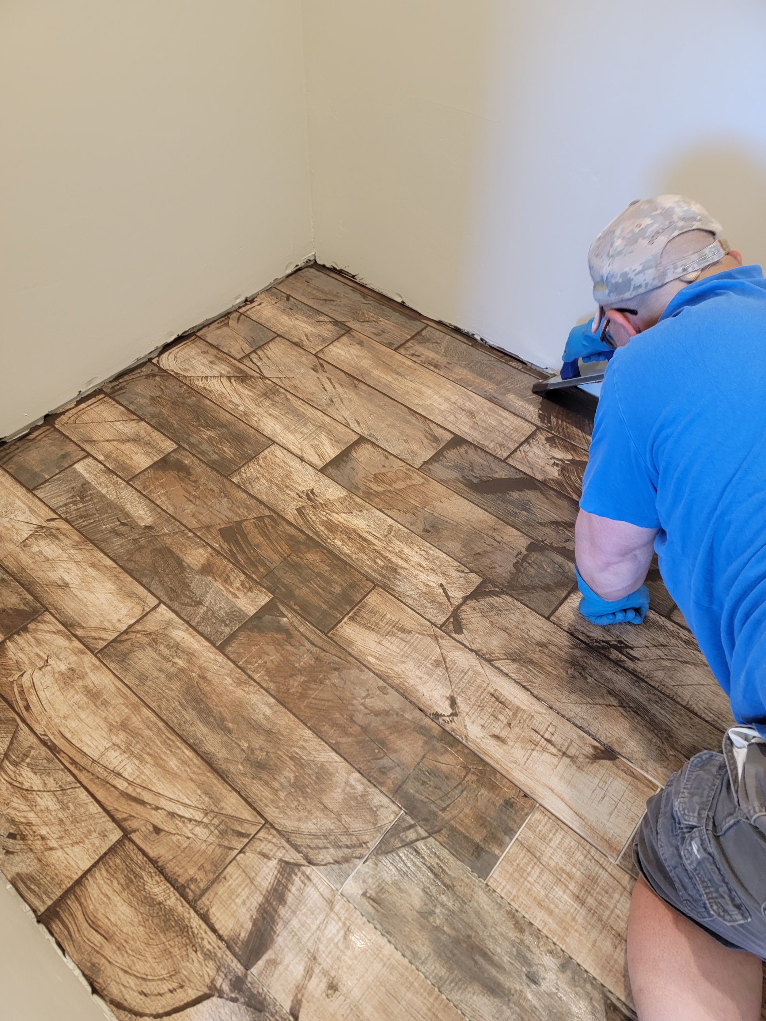 Person installing or repairing wooden flooring in a room with plain beige walls.