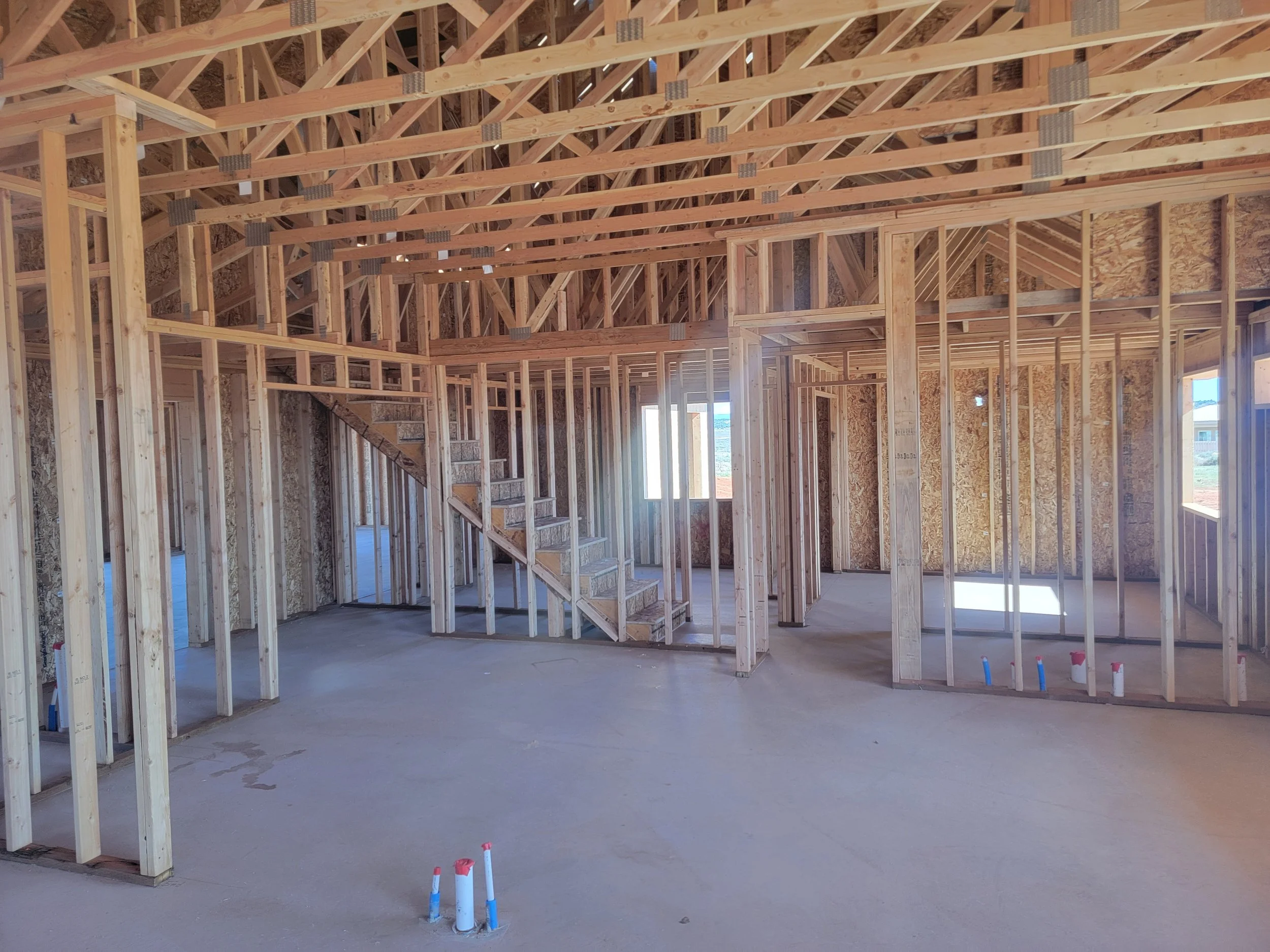 The interior of a house under construction with exposed wooden framing, stairs, and unfinished walls.