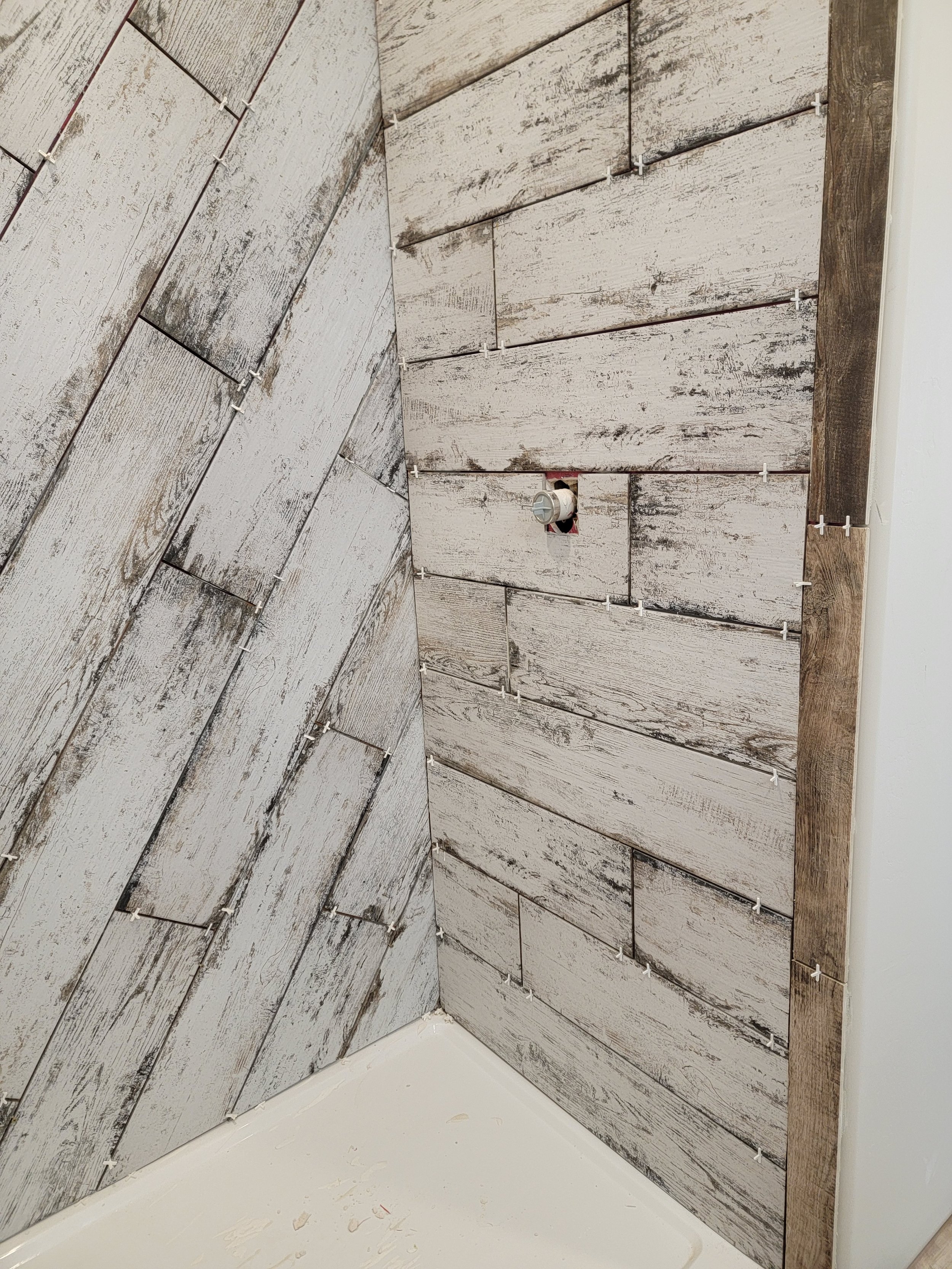 A corner of a room showing wooden wall panels with a distressed white finish, a light brown border, and a partially installed electrical outlet with visible wiring.