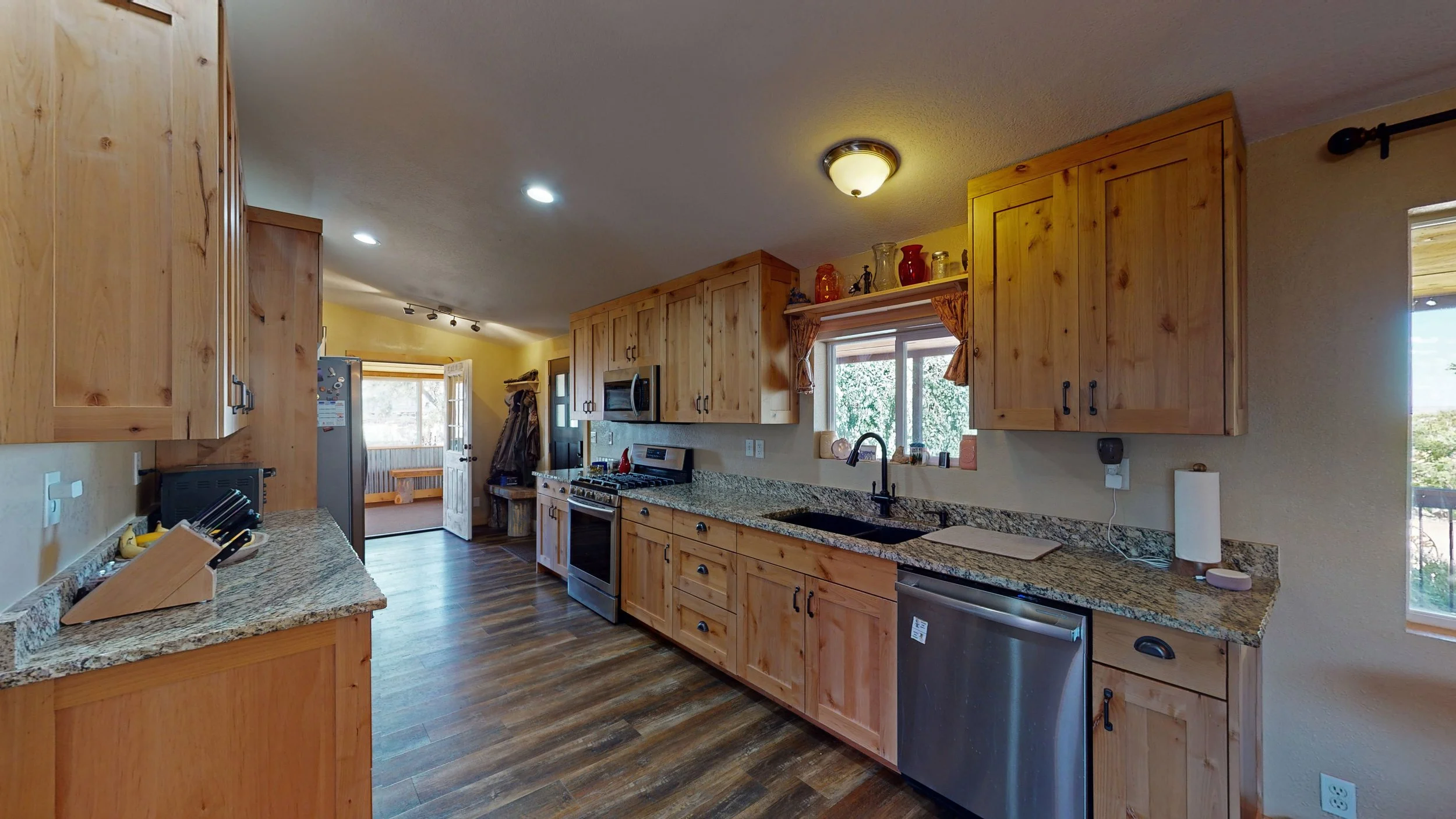 A kitchen with wooden cabinets, granite countertops, a stainless steel oven, microwave, and dishwasher, a window above the sink, and a door leading outside.