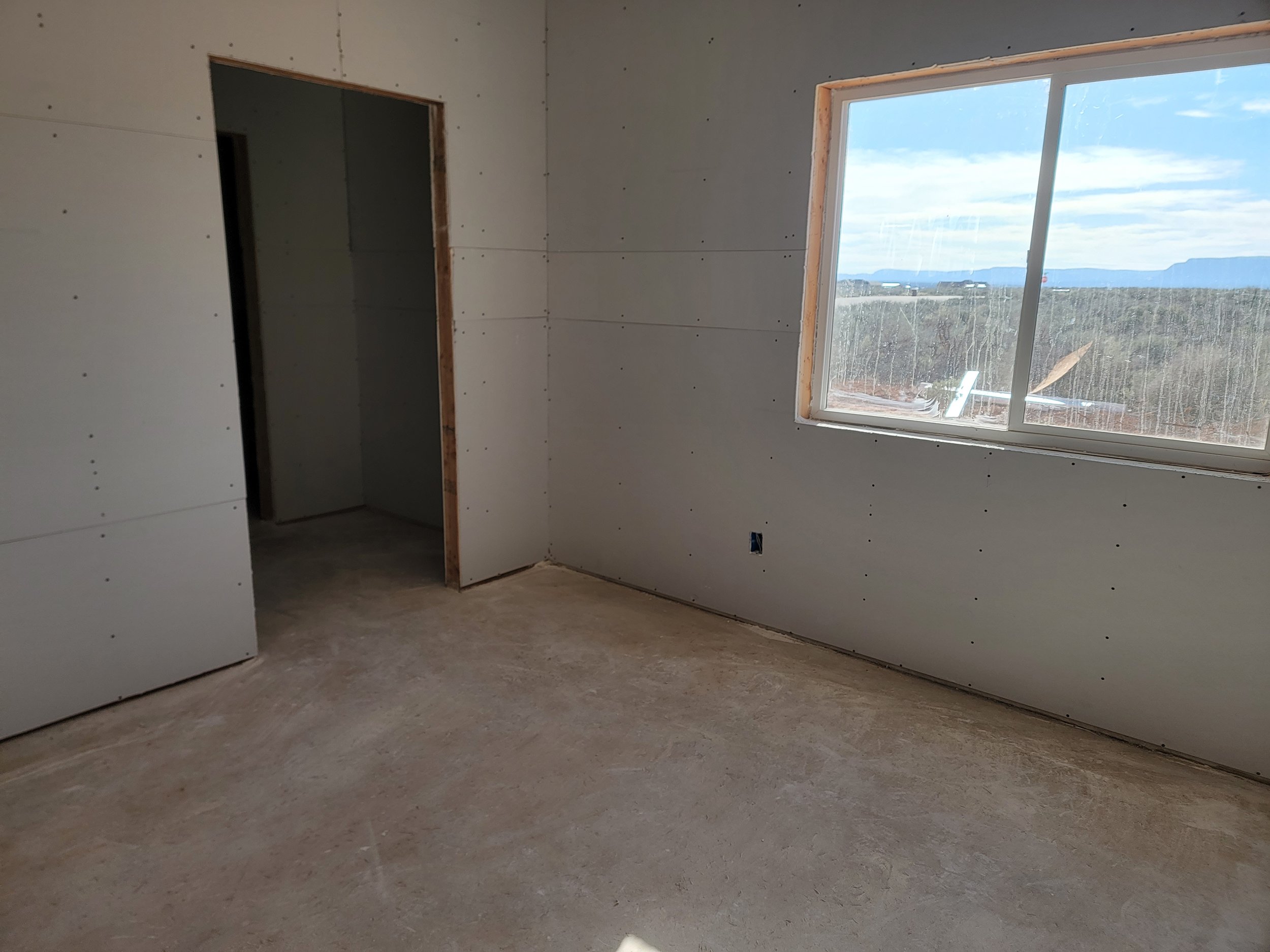 An unfinished room with drywall installed on the walls and a large window showing a landscape with mountains in the background.