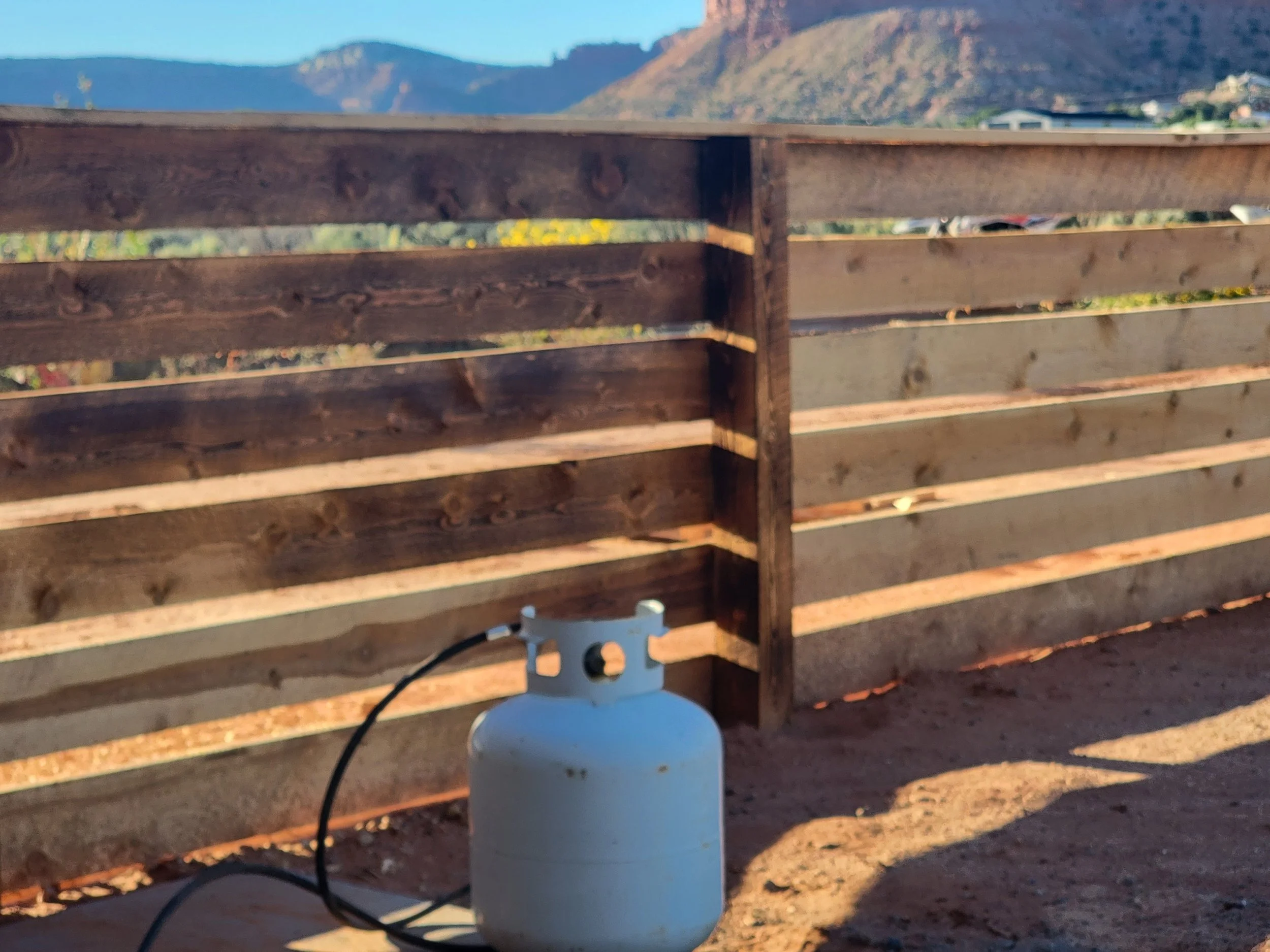 A wooden outdoor railing with a power outlet and cords in front of a mountain landscape in the background.