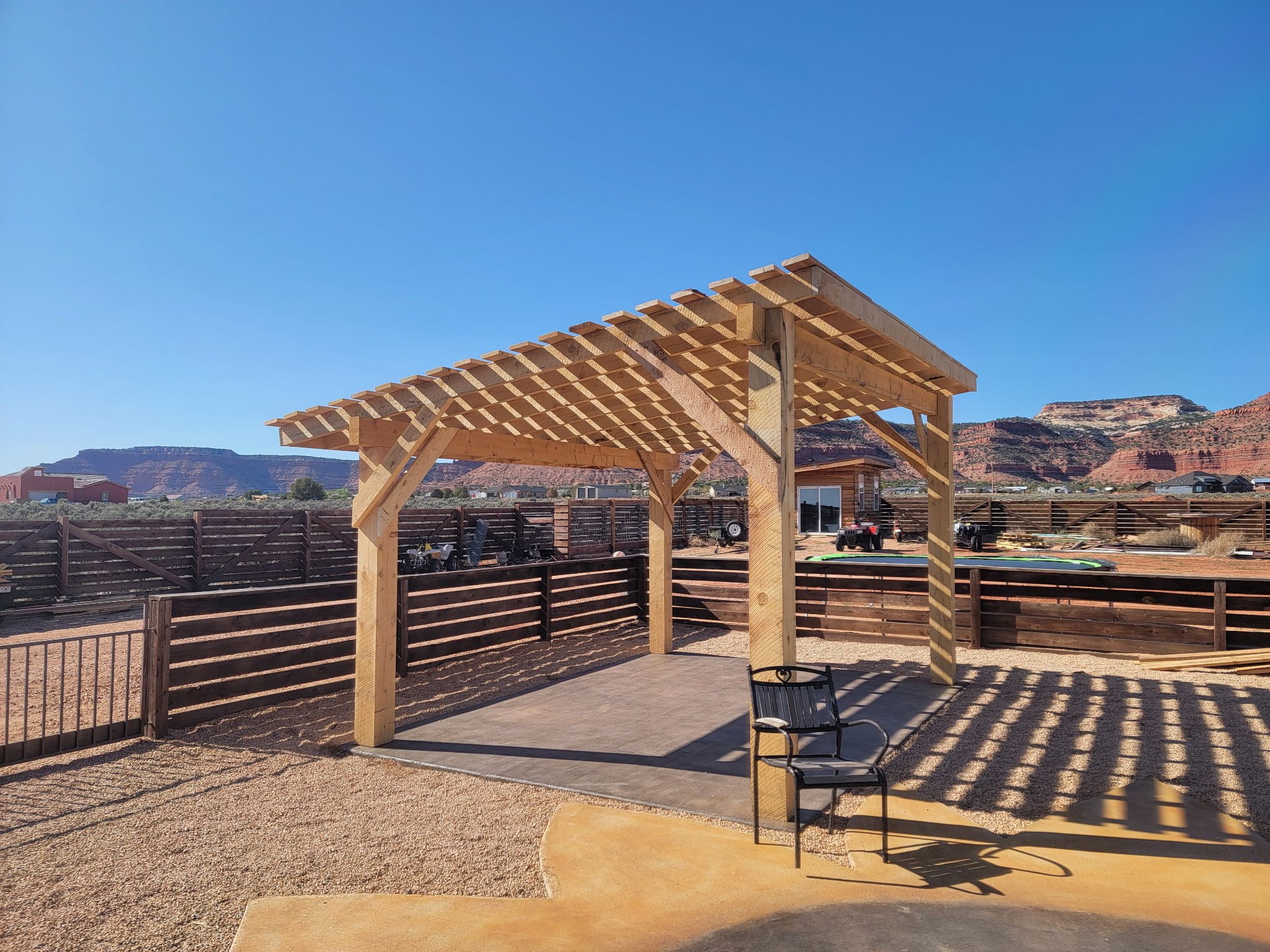 Wooden pergola under construction in backyard with mountains in background and some patio furniture.