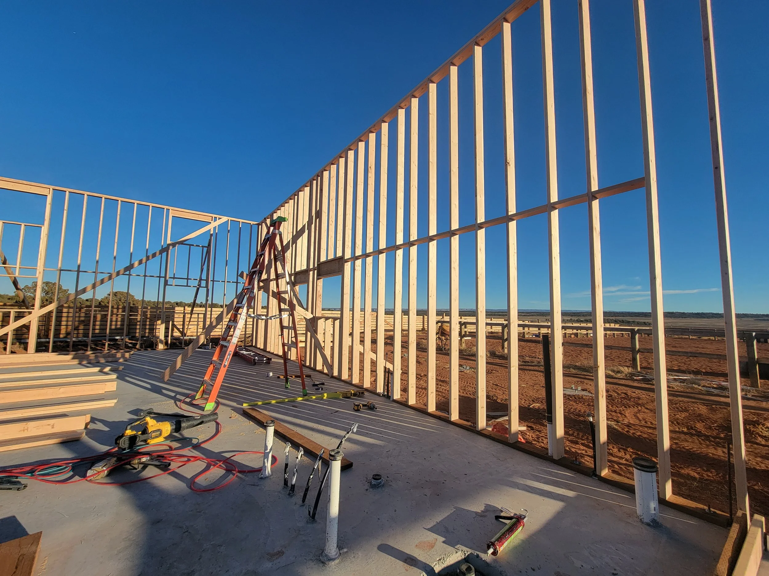 Construction site with wooden framing for a building under construction, tools, and a ladder, with a clear blue sky in the background.