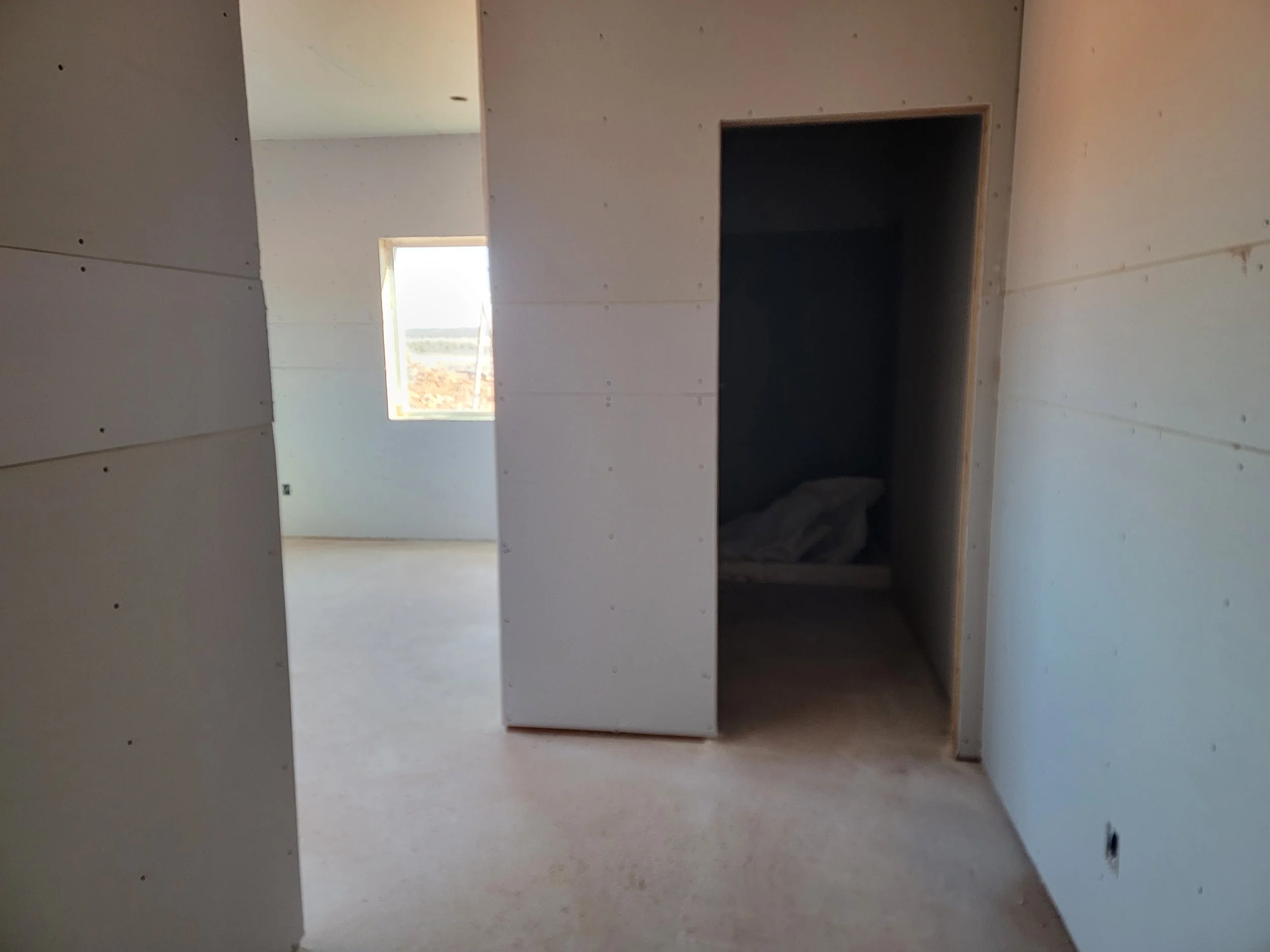 Interior view of a room under construction with unfinished drywall walls, an open doorway, and a window letting in natural light.