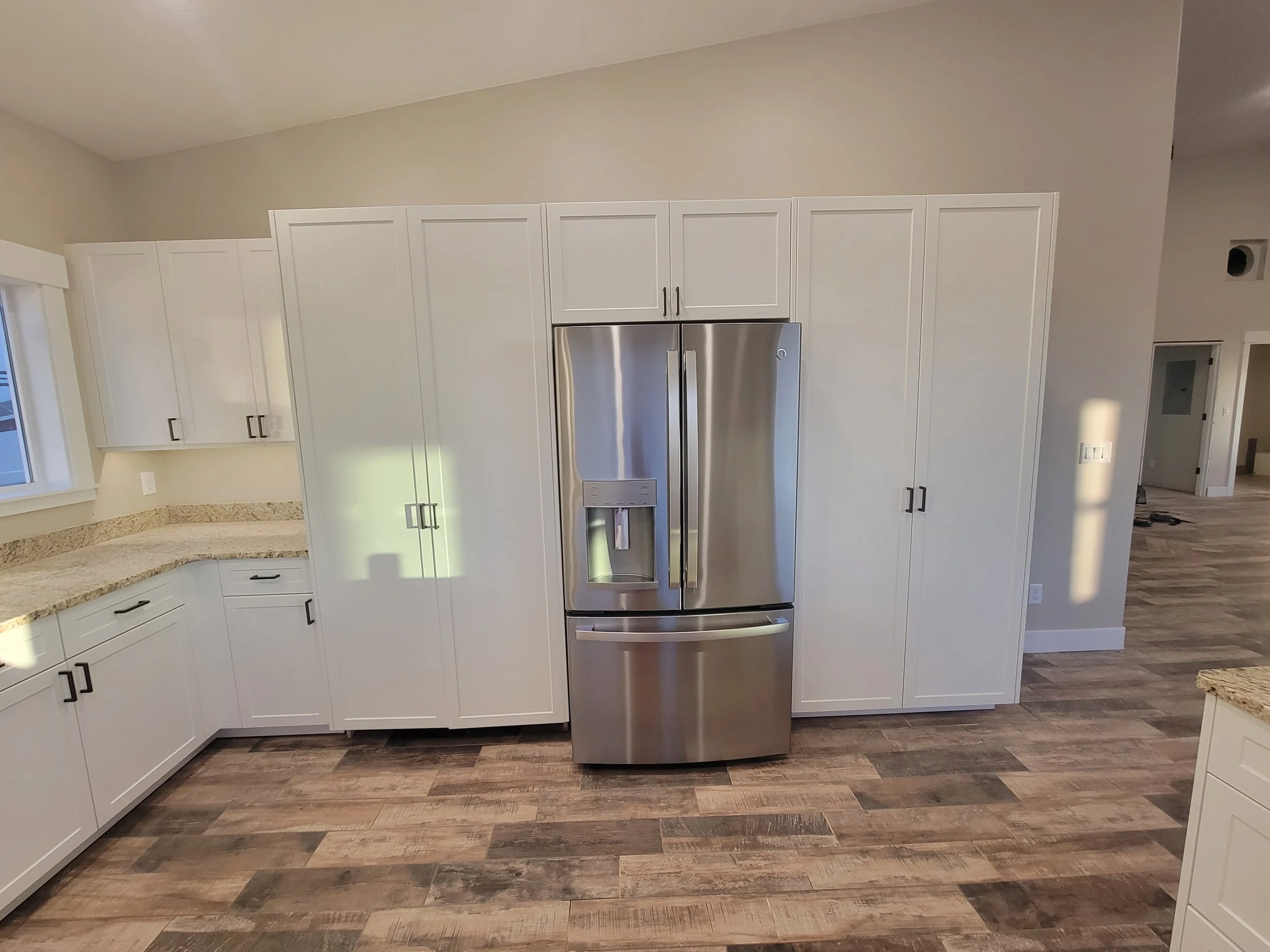 Modern kitchen with white cabinets, stainless steel refrigerator, wood flooring, and beige countertops.