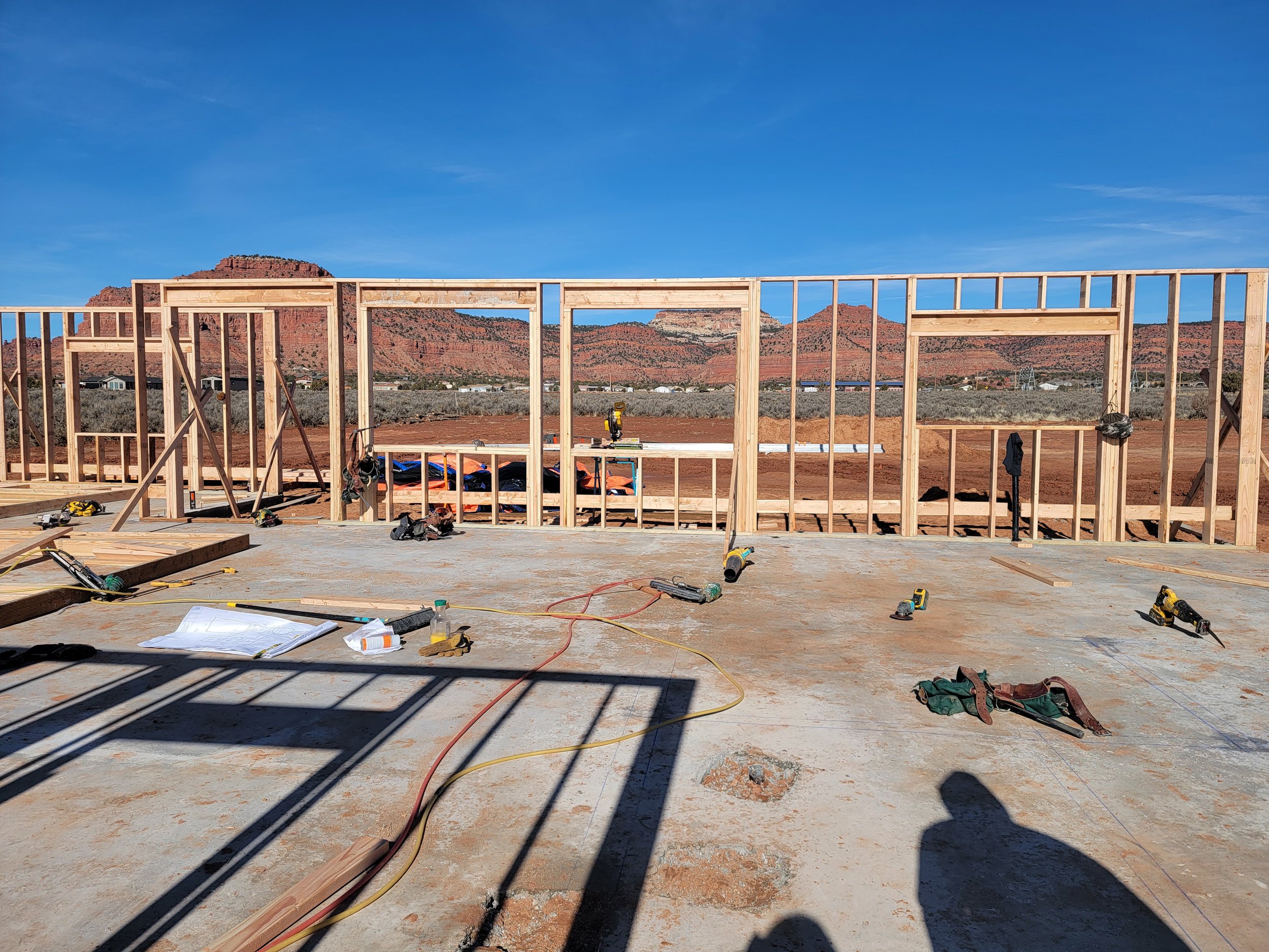 Construction site with a wooden framework for a building, tools, and cables. Mountain landscape and blue sky in the background.