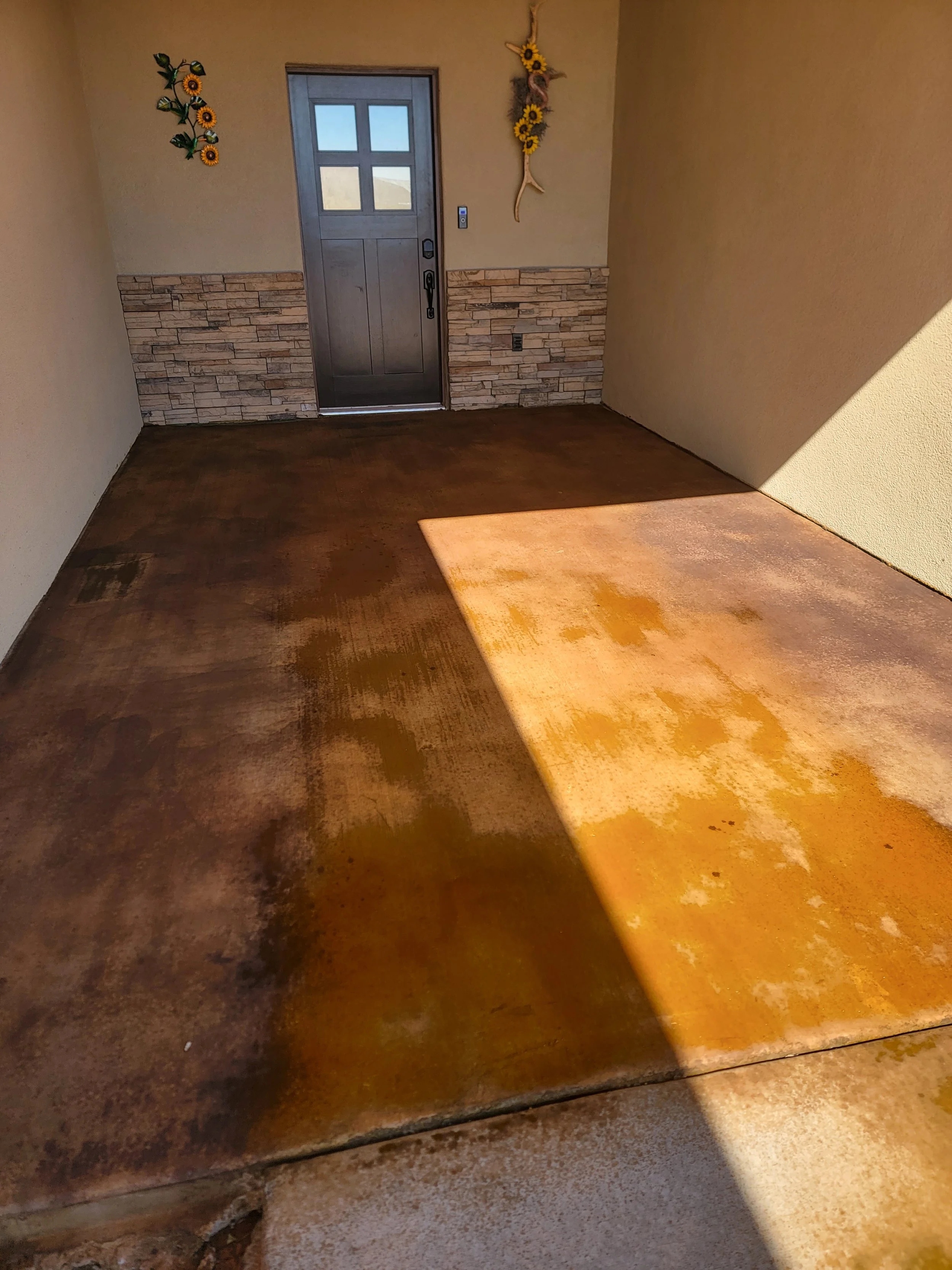 Interior view of a doorway with a wooden door and window, with decorative sunflower and rustic wall hangings, and a partially completed hardwood floor.