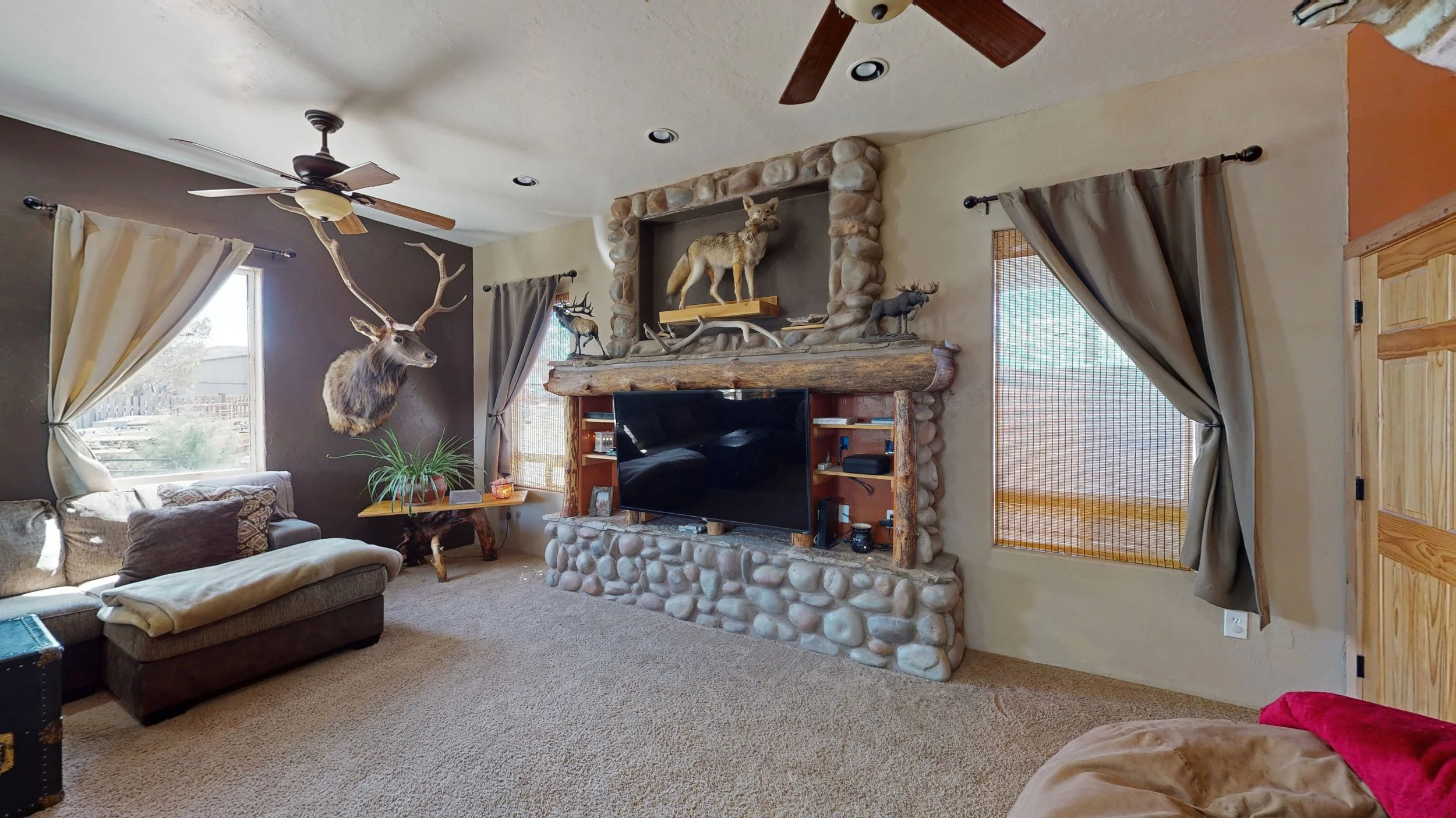 Living room with a stone fireplace, mounted deer head, animal figurines, a TV, and windows with curtains.