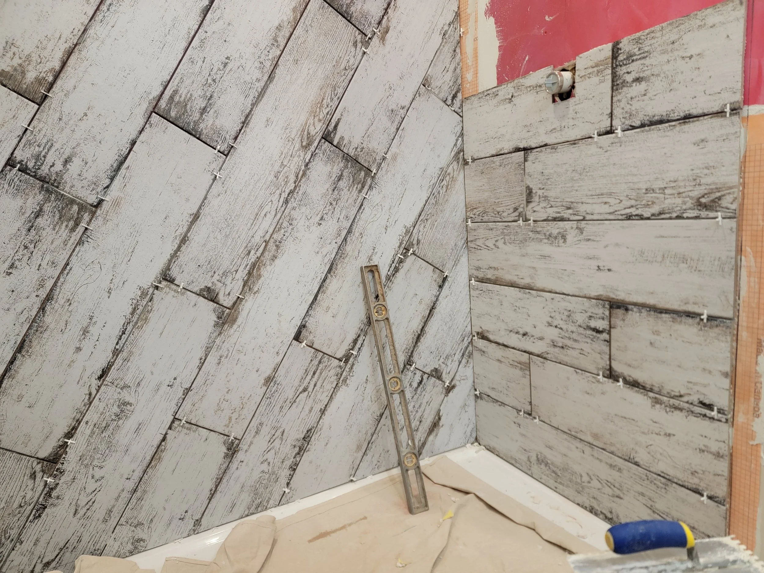 Installing weathered wooden planks on a wall with tiles, using spacers and a level for alignment in construction or renovation.