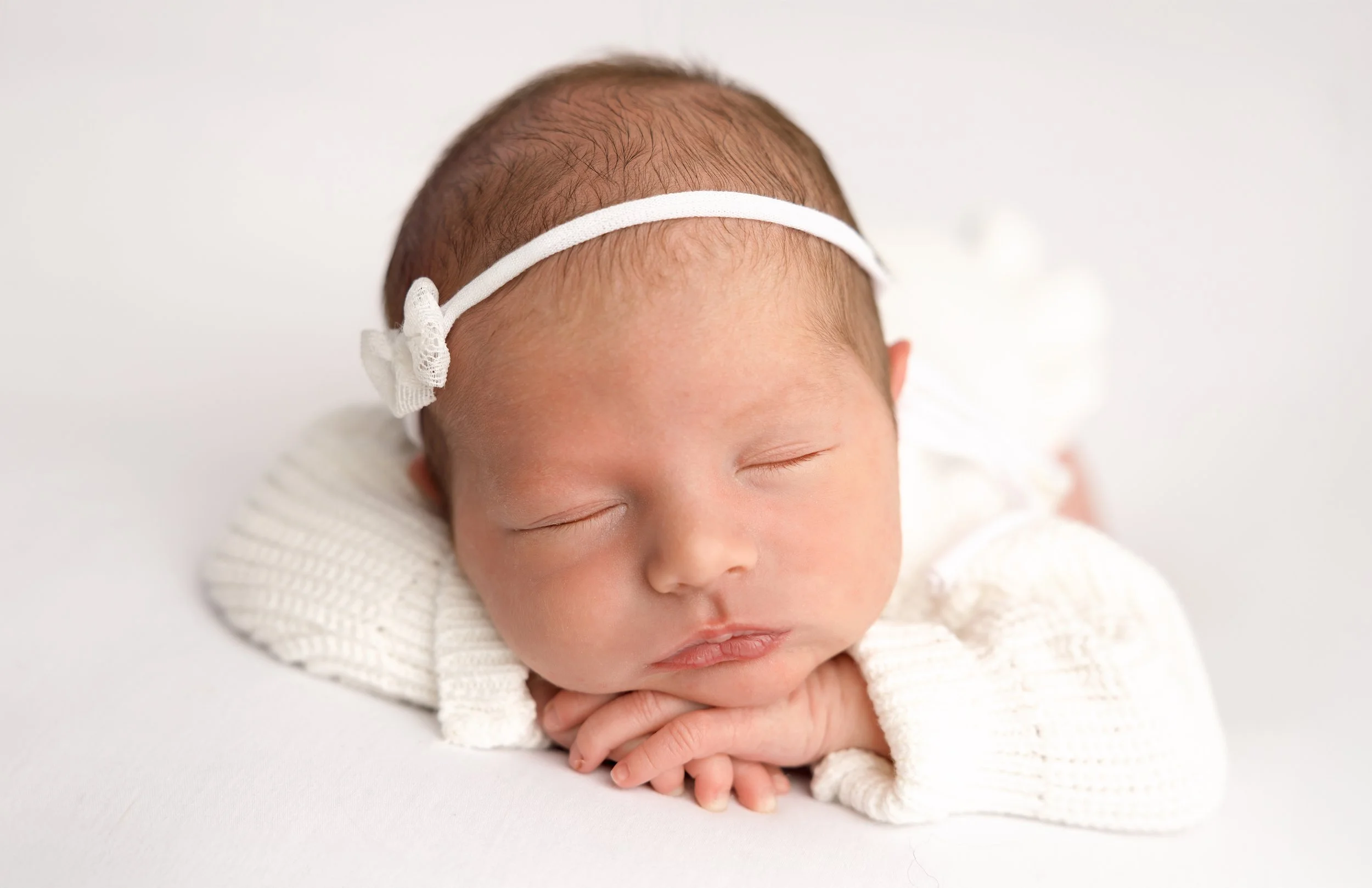 A sleeping newborn baby with a headband, resting on a white surface.