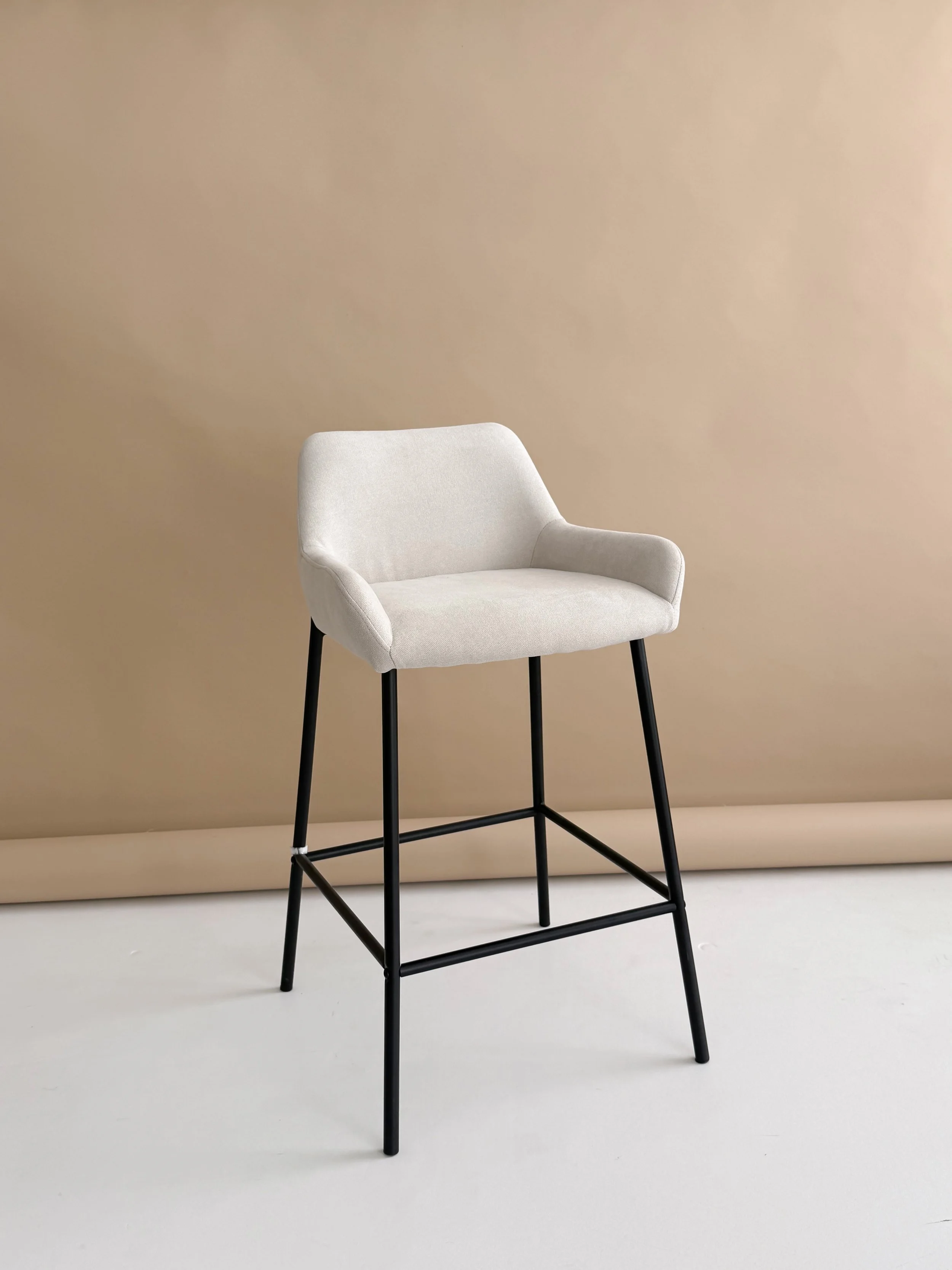 A white modern lounge chair with black metal legs positioned in front of a beige wall, on a white floor.