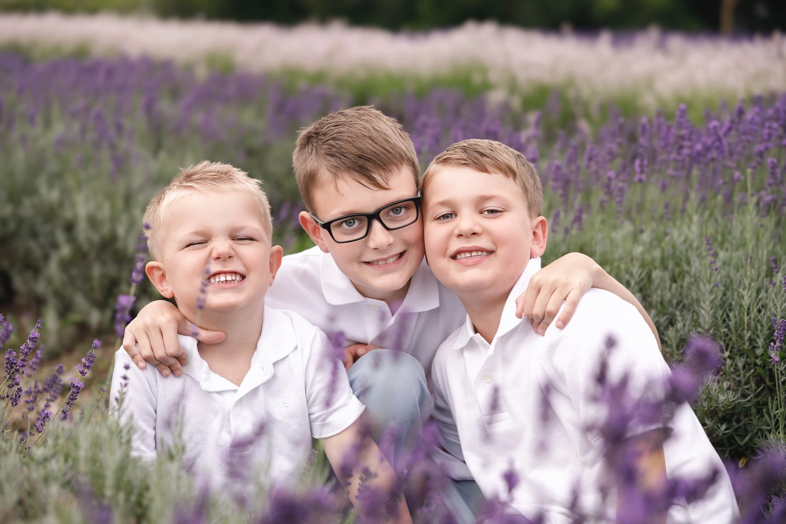 Three boys smiling and hugging in a lavender field.