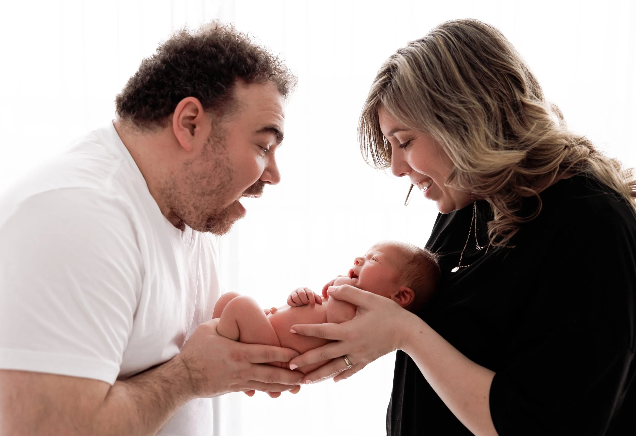 A man and woman smile as they hold a newborn baby, looking lovingly at the infant.
