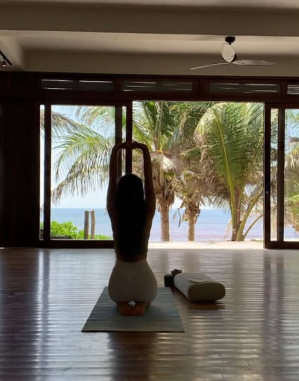 Woman doing yoga on her mat with palm trees in the background.