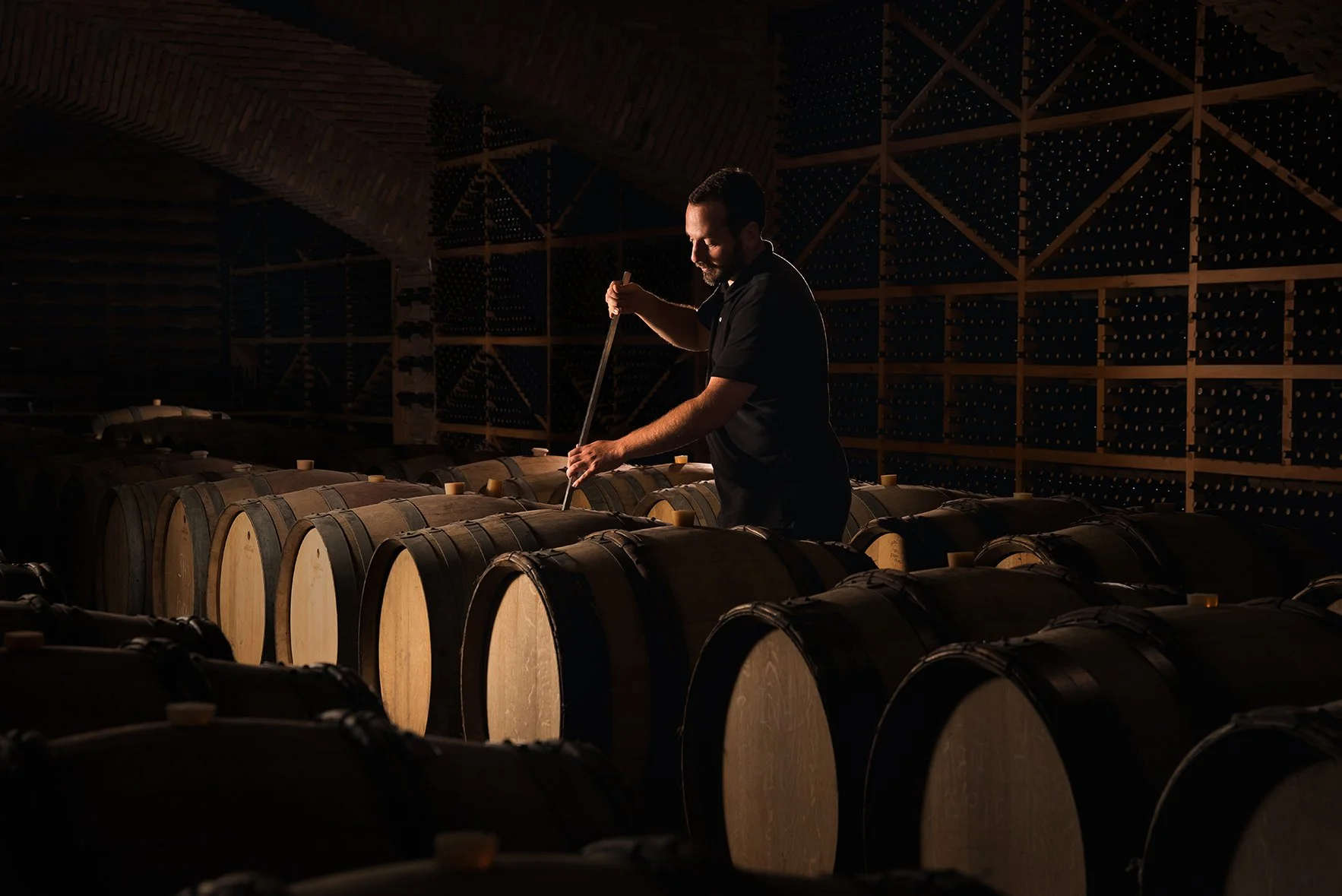 A man inspecting wine barrels in a dimly lit cellar.
