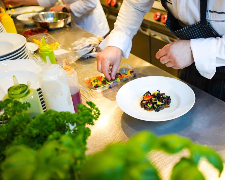 Chef garnishing a plated dessert with colorful candies in a professional kitchen setting.