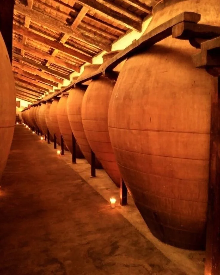 Row of large wooden wine barrels in a dimly lit cellar with candles along the floor.