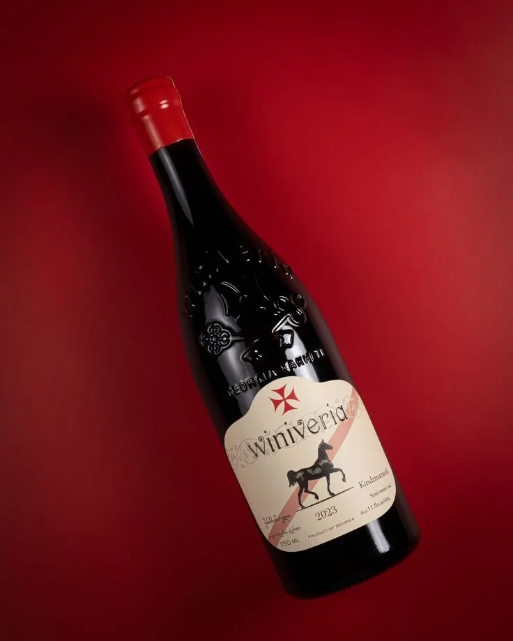 A bottle of red wine labeled 'Winiveria' with a vintage-style label featuring a leopard and a red star, against a red background.
