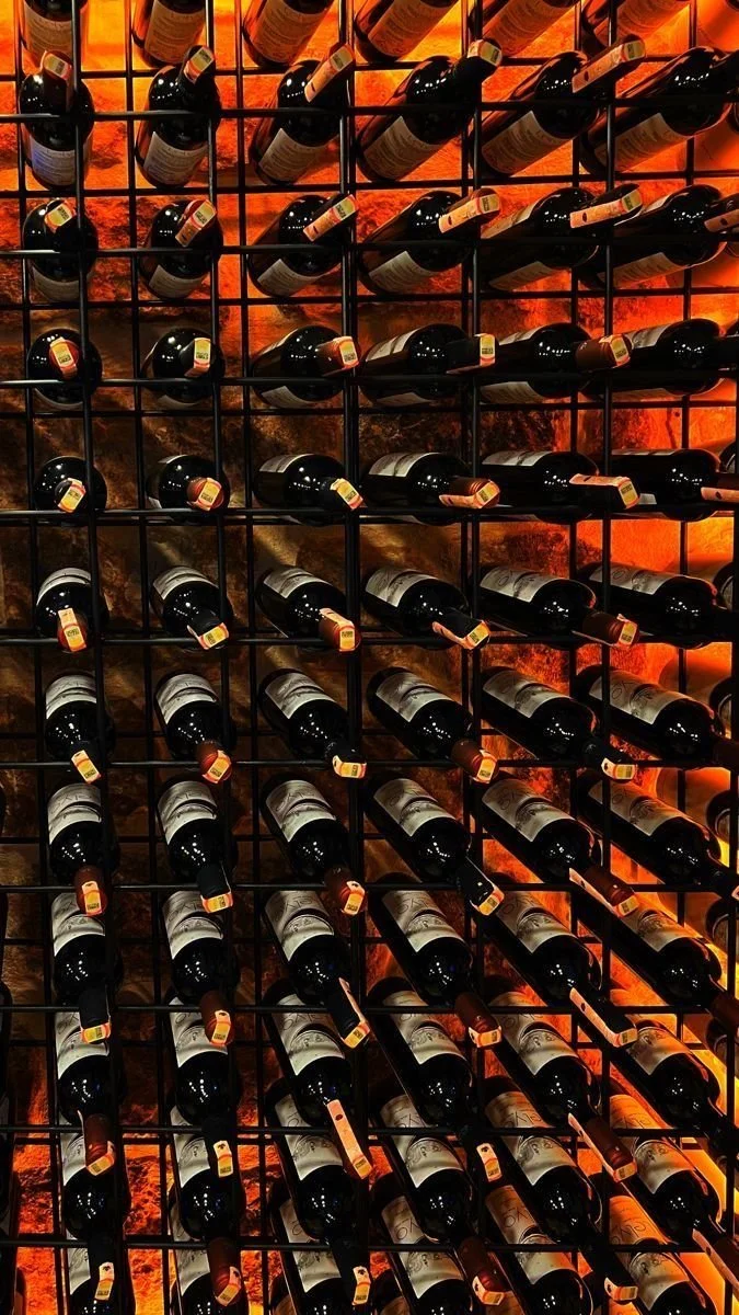 A wine rack filled with bottles organized on horizontal and vertical slots, illuminated by warm orange lighting from behind.