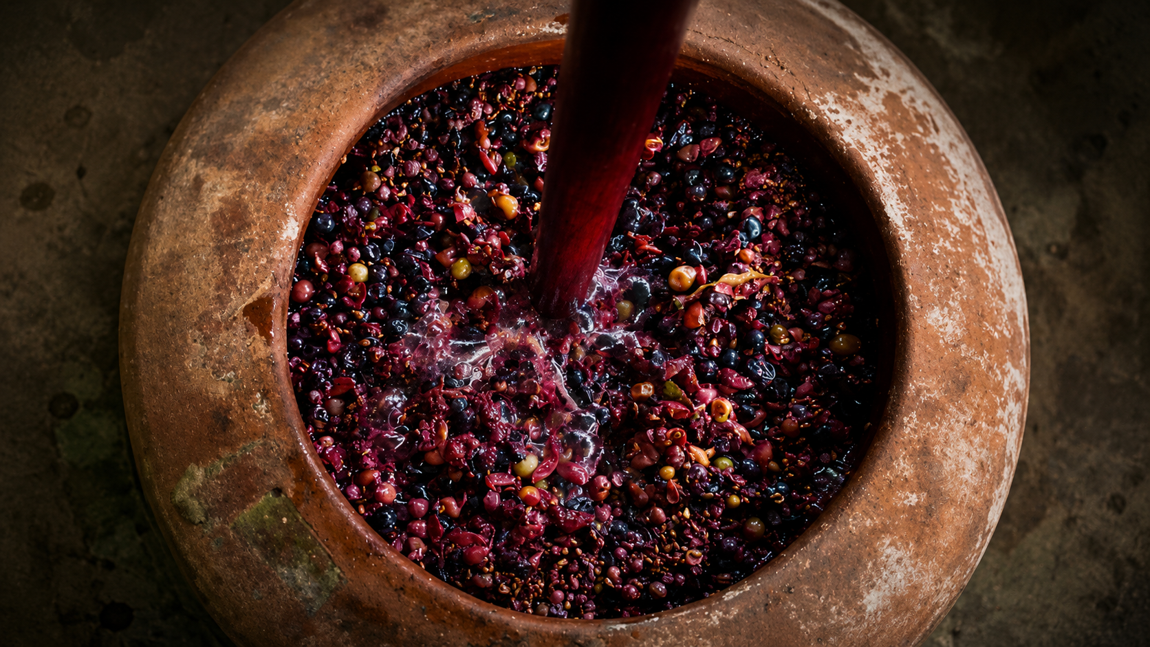 A large earthenware jar filled with crushed grapes and juice, with a wooden pestle or crusher in the center, used for wine making or grape processing.