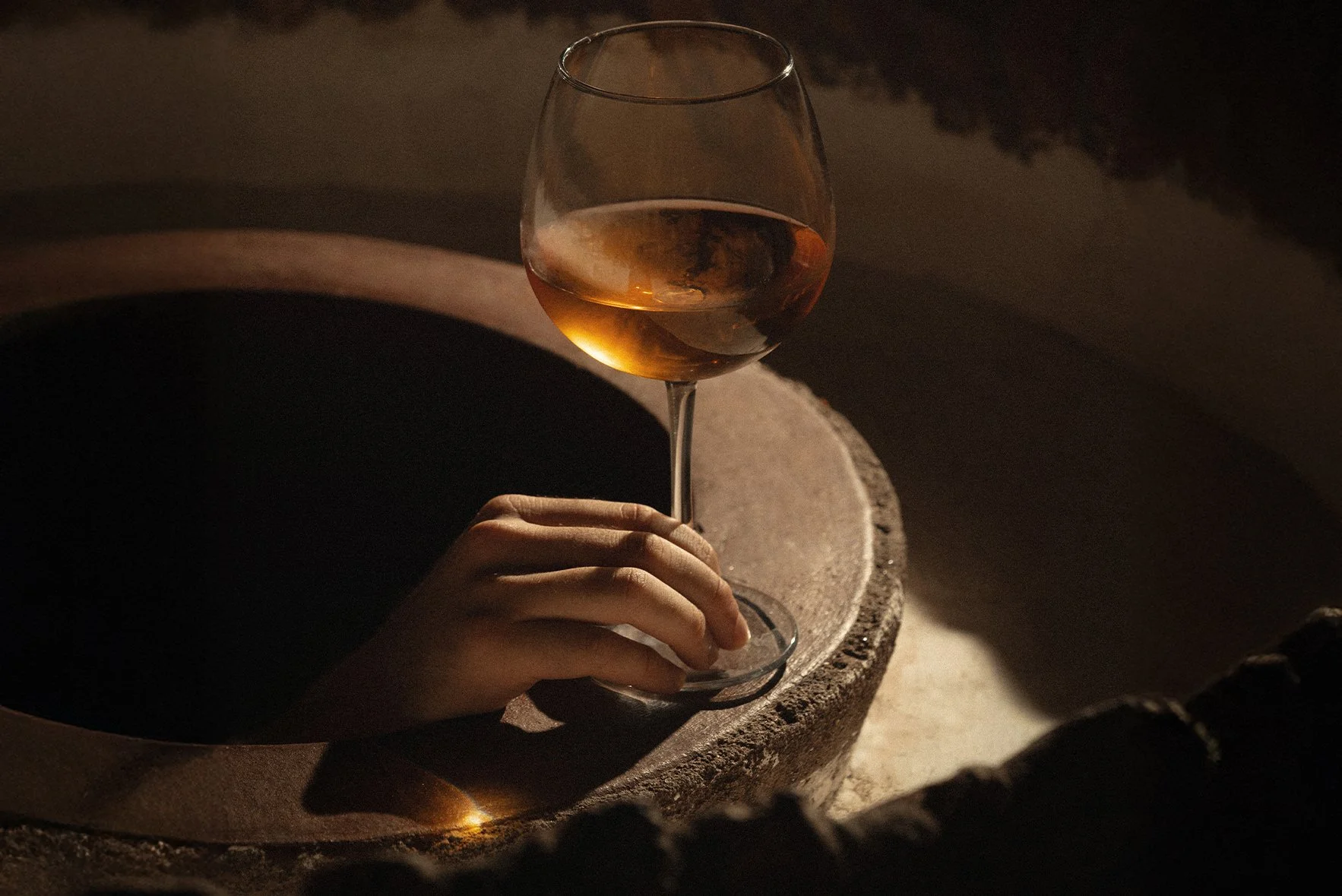 A hand holding a glass of rosé wine with a dark background and soft lighting.