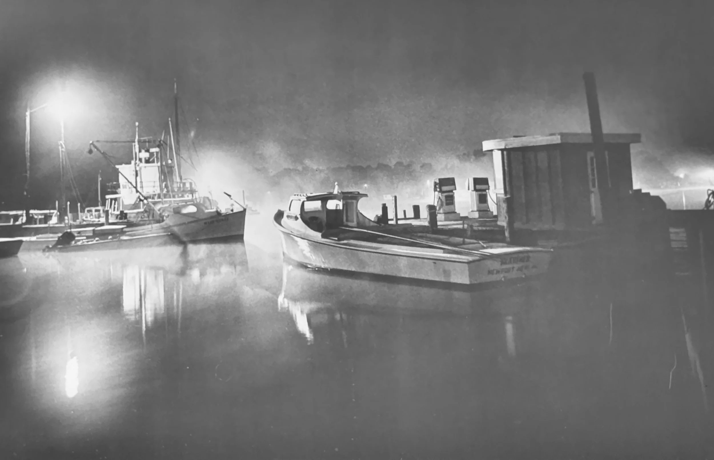 Black and white image of two docked workboats on a foggy night.