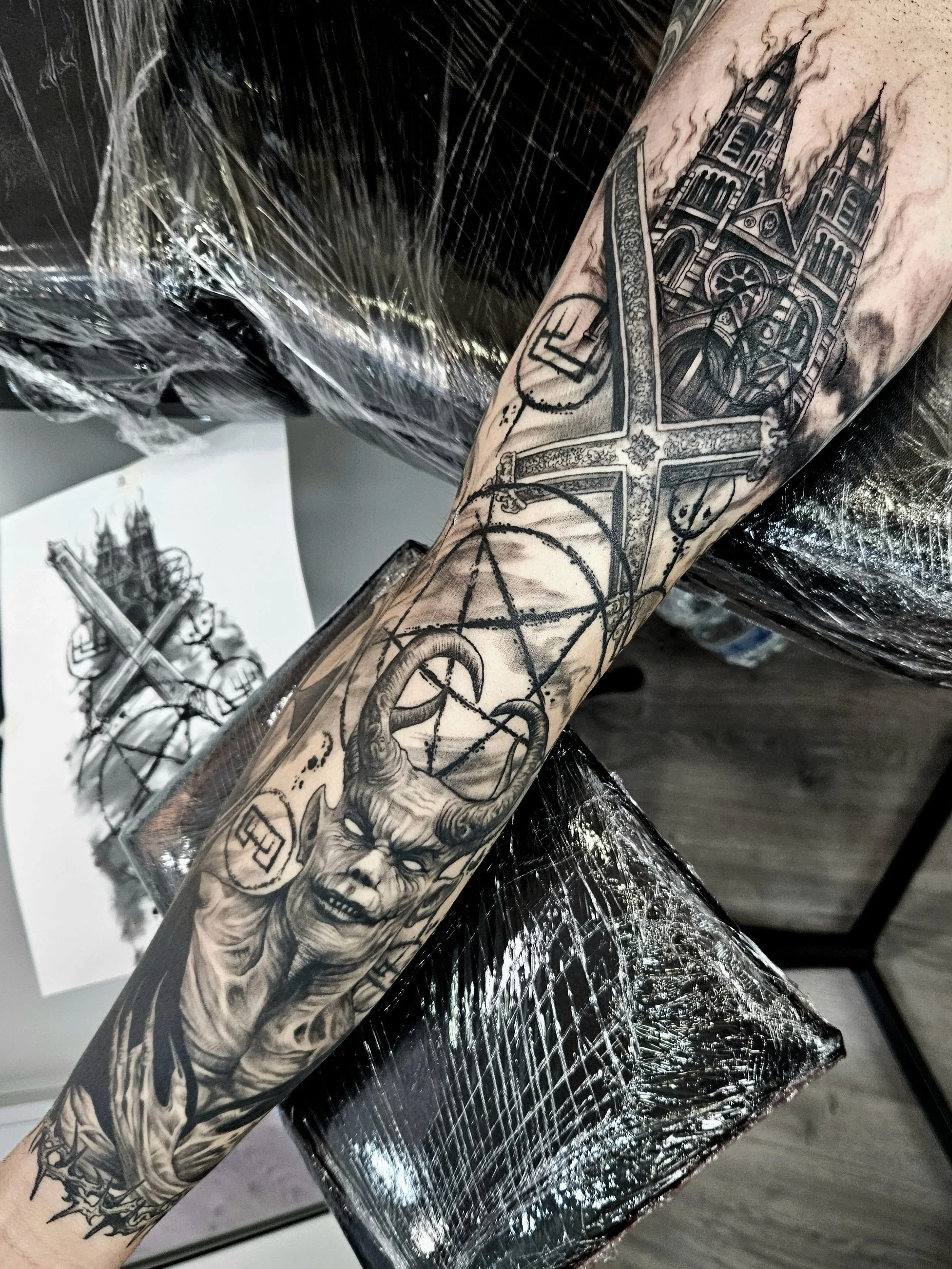 A tattoo sleeve featuring a gothic cathedral, a detailed sword, a mythological creature, and geometric designs on a person's arm.
