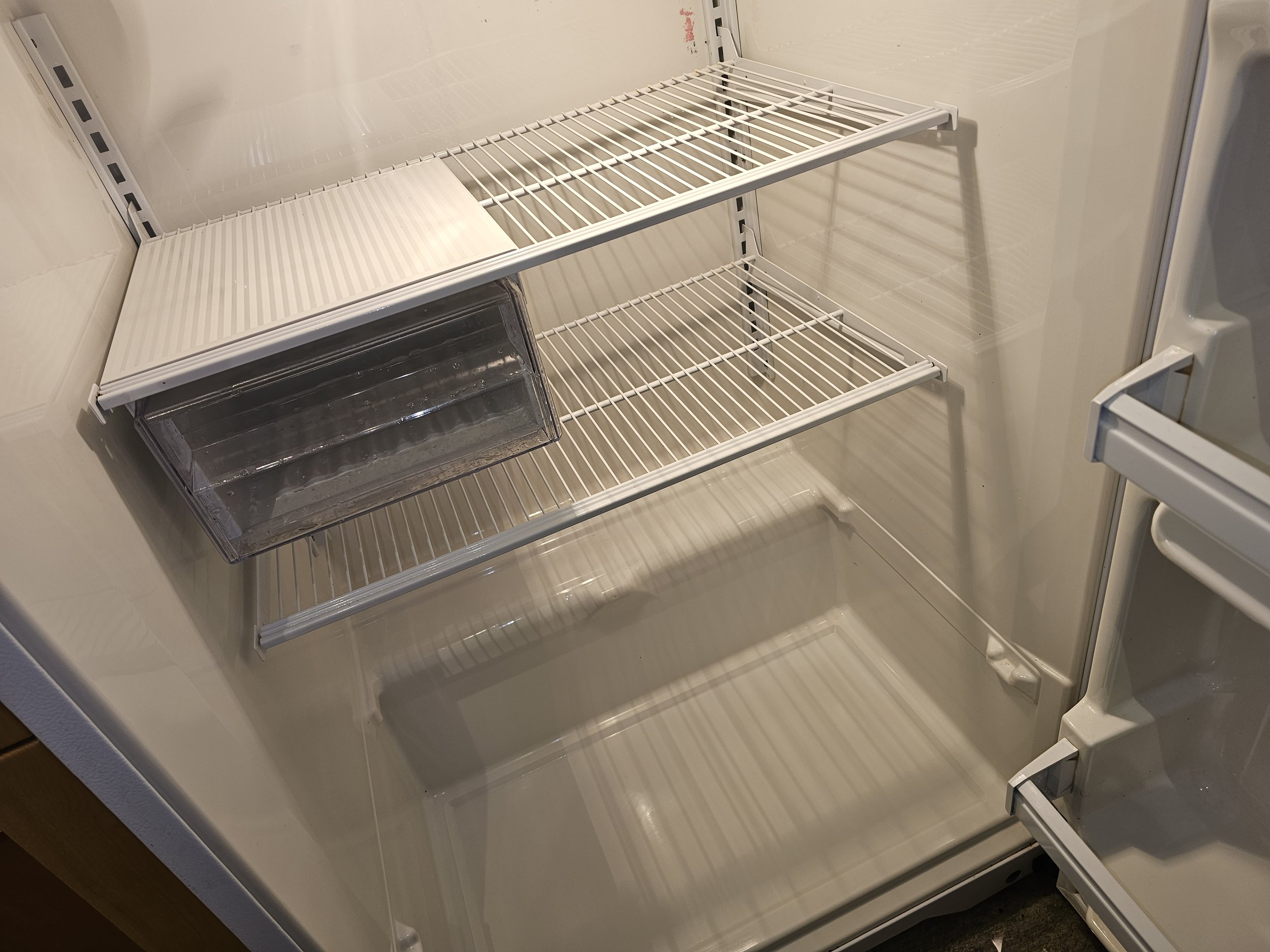 Empty white refrigerator interior with three wire shelves and a small clear plastic drawer at the bottom.