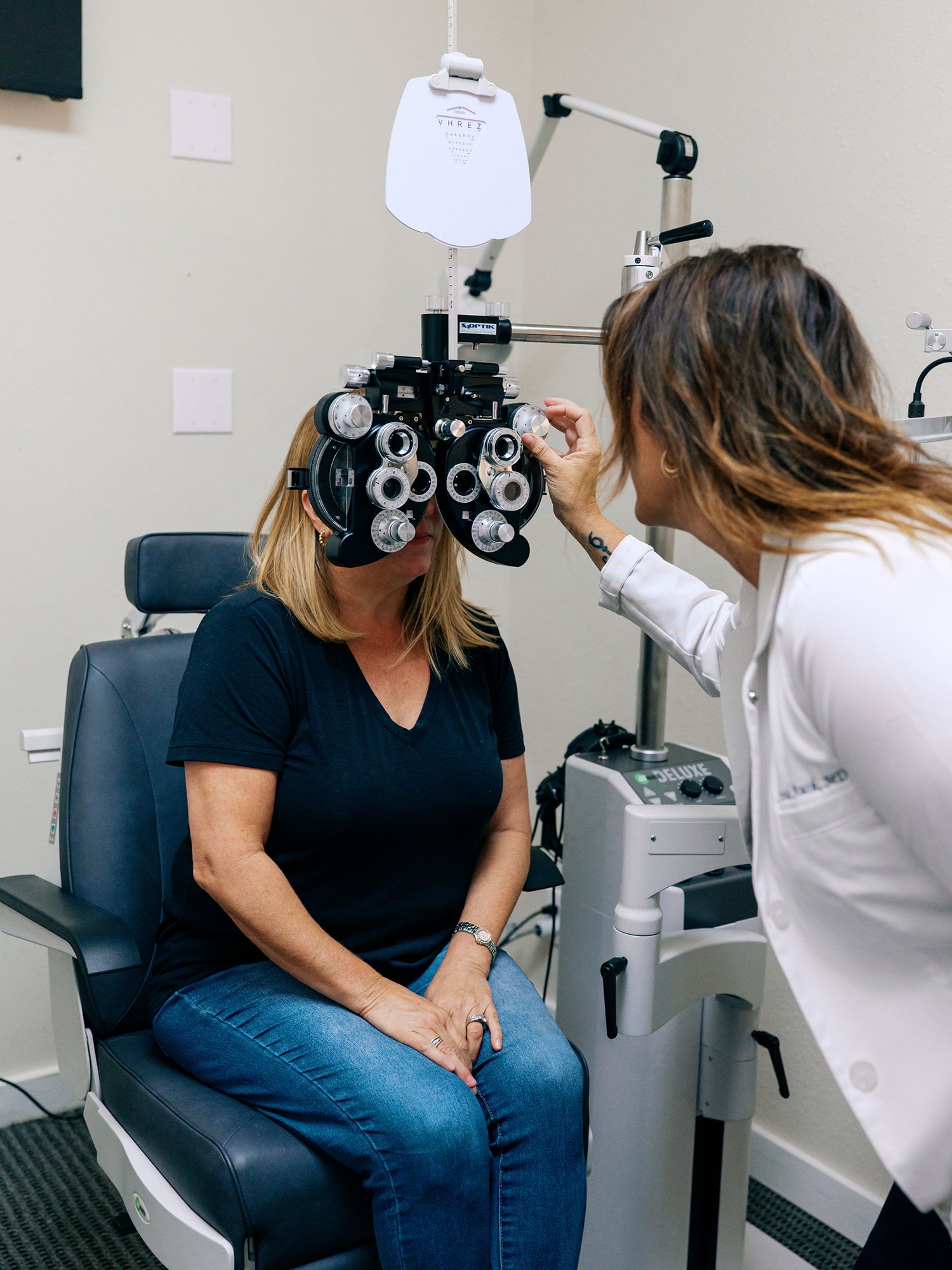 Optometrist conducting an eye exam on a woman using a phoropter in a clinic.