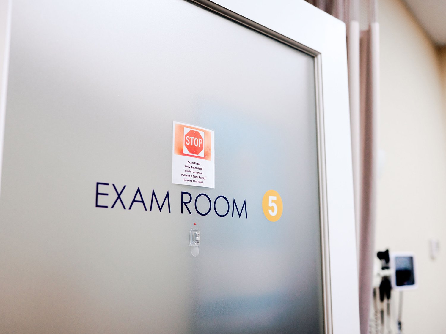 Hospital examination room door with signage that reads "EXAM ROOM 5" and a smaller sign that says "STOP Exam Room Only Authorized Clinic Personnel Patients & Their Family Beyond This Point."
