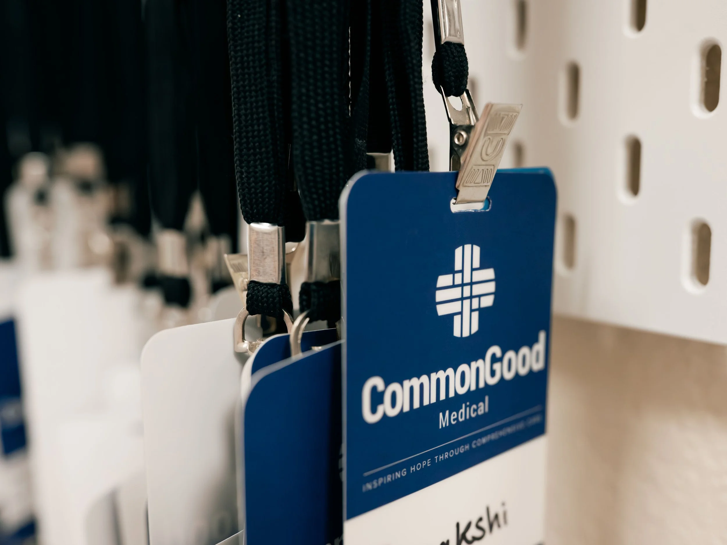 Close-up of black lanyards with silver clips hanging from hooks on a white pegboard with yellow and gray tones, including a blue badge with part of the logo visible.