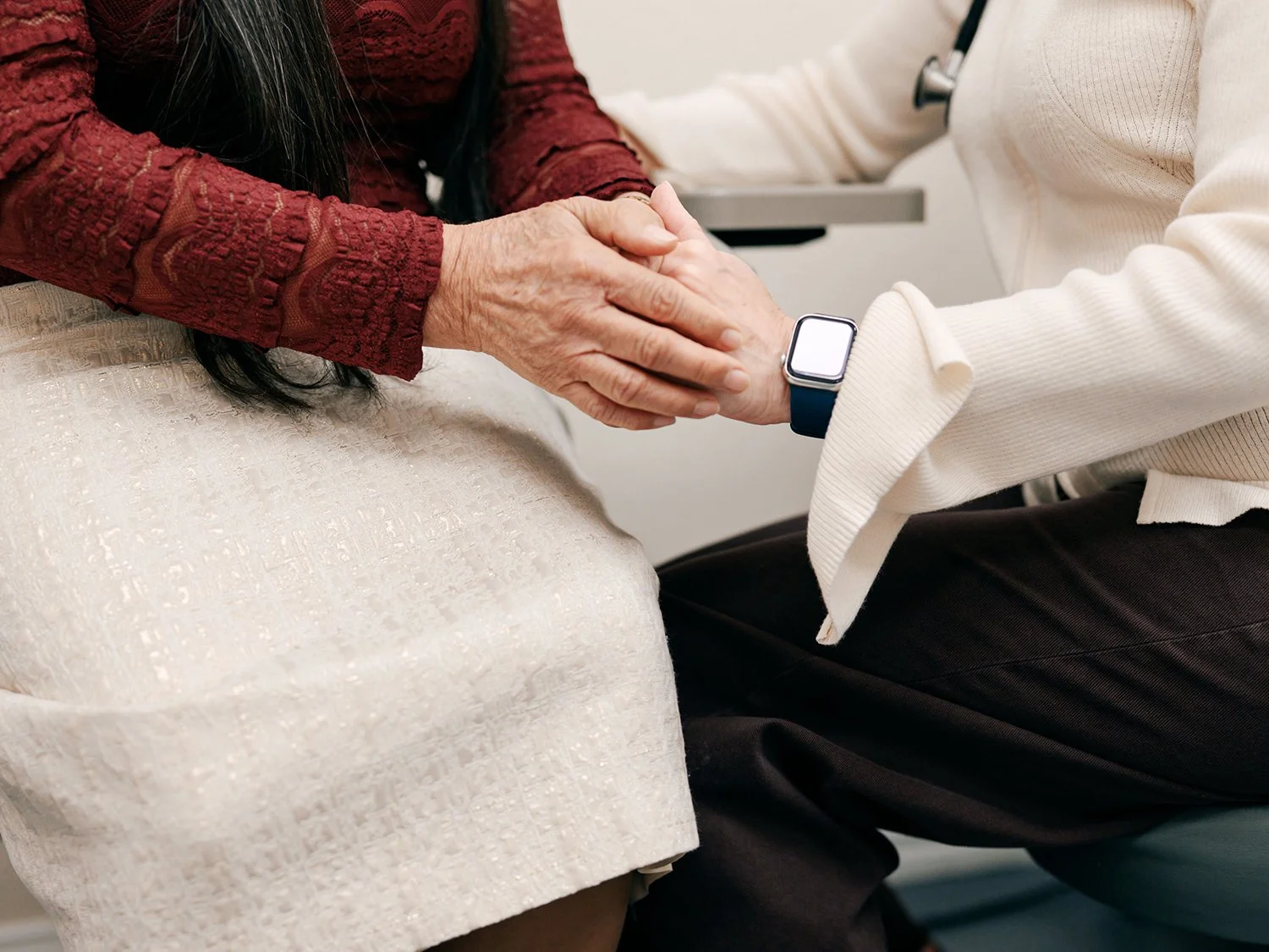 Two people holding hands during a healthcare appointment, with one person wearing a smartwatch on their wrist.
