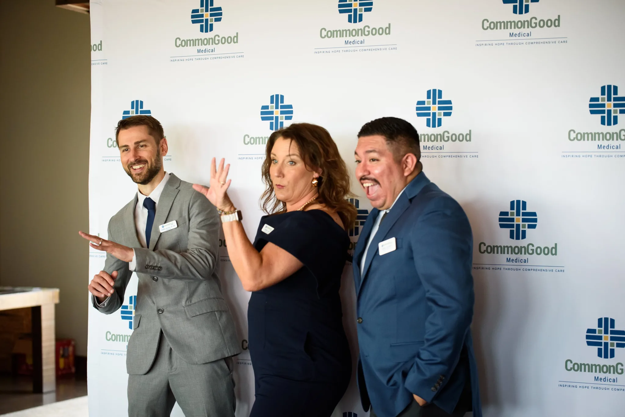 Three people standing in front of a CommonGood Medical backdrop, smiling and joking, dressed in professional attire.