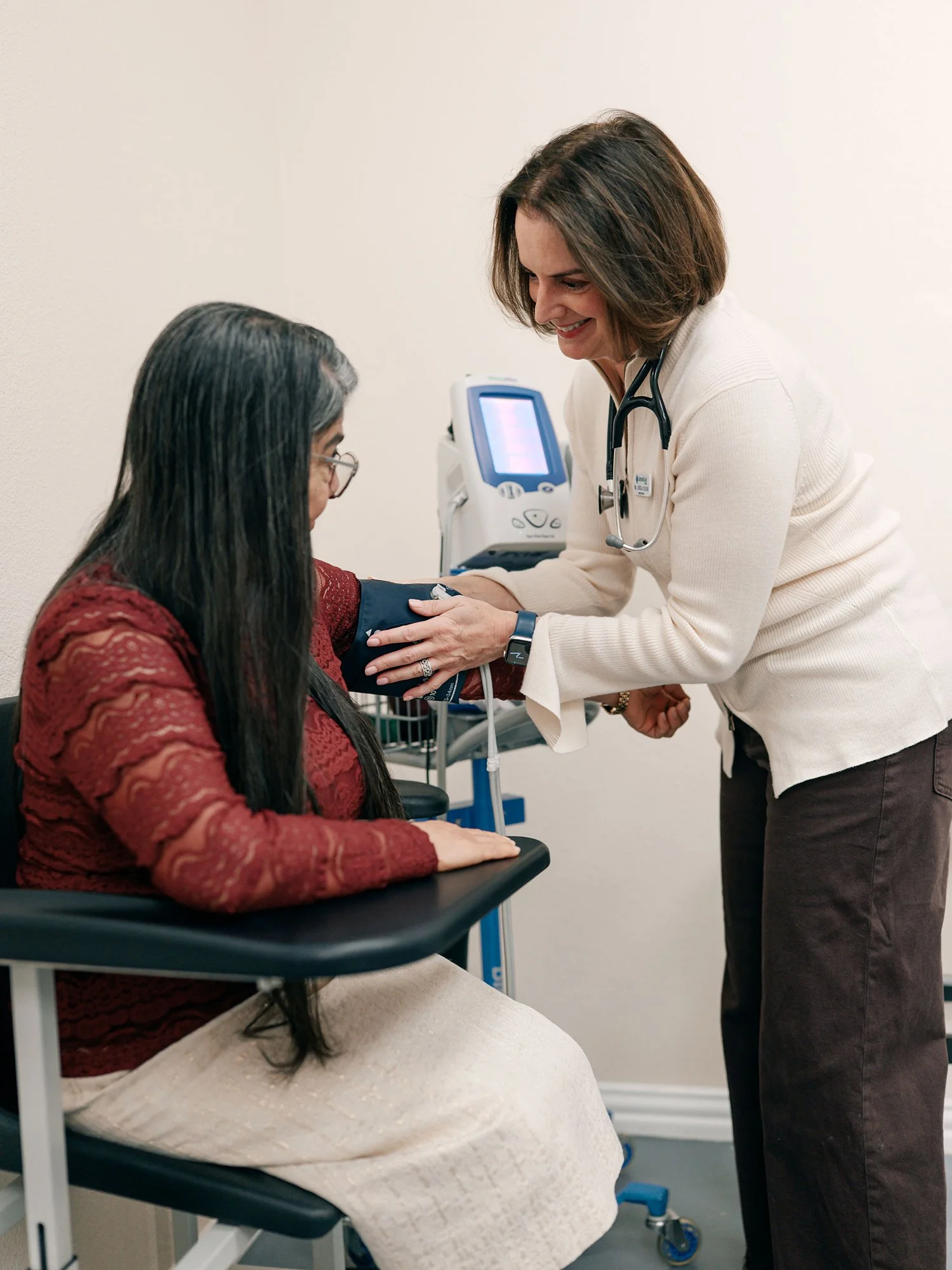A healthcare professional taking a woman's blood pressure in a medical clinic room.