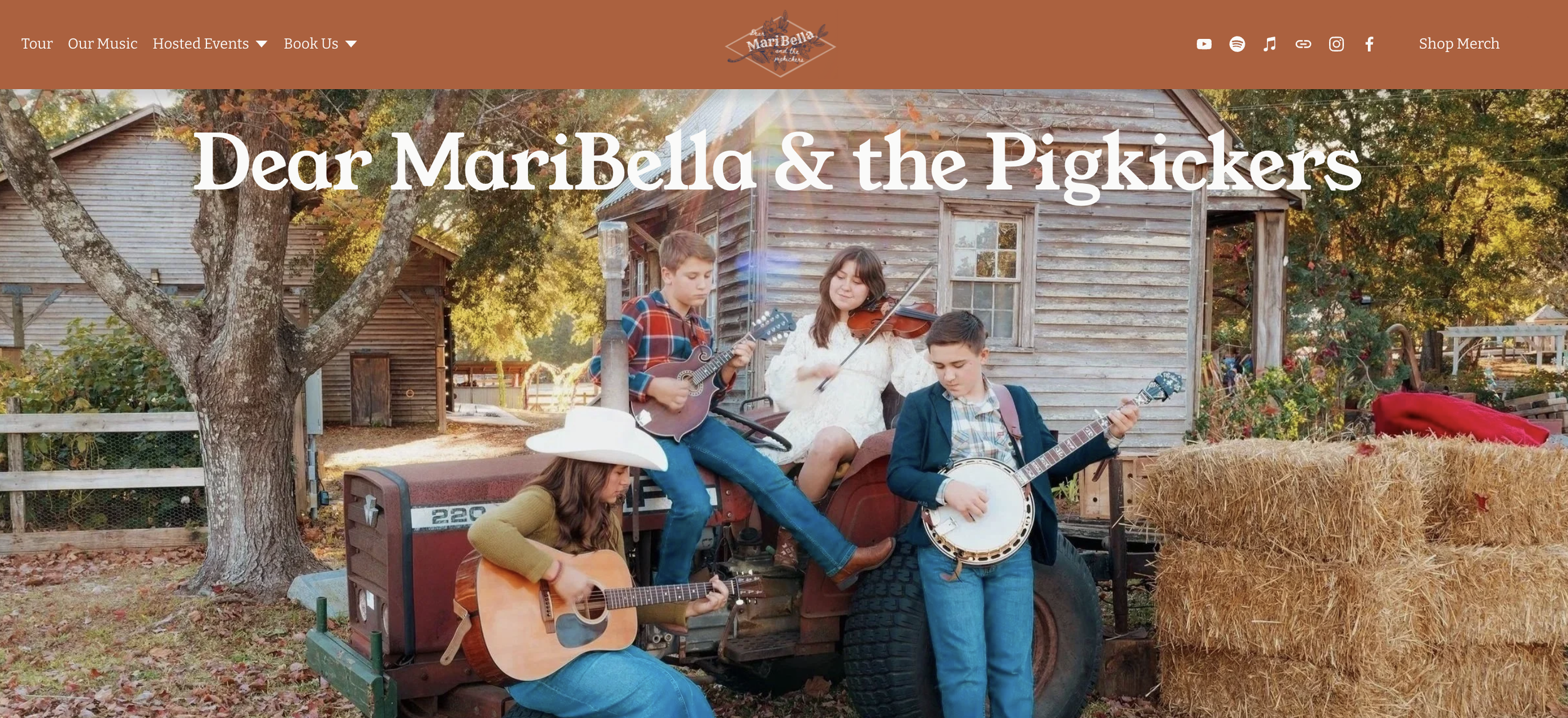 Four musicians playing musical instruments outdoors near a weathered shed, with hay bales and autumn foliage. Click to view the website.