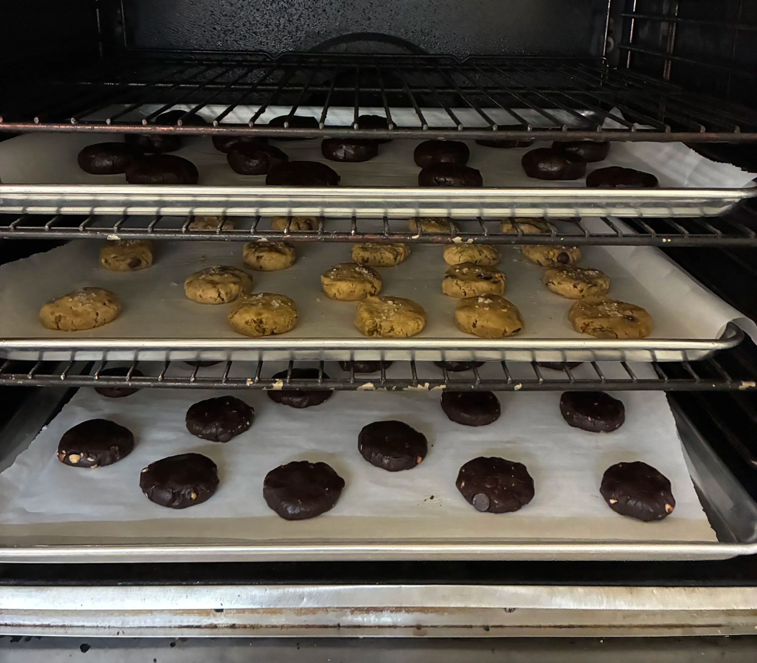 Three baking sheets of Rae’s Salted Sweets cookies baking in the oven.