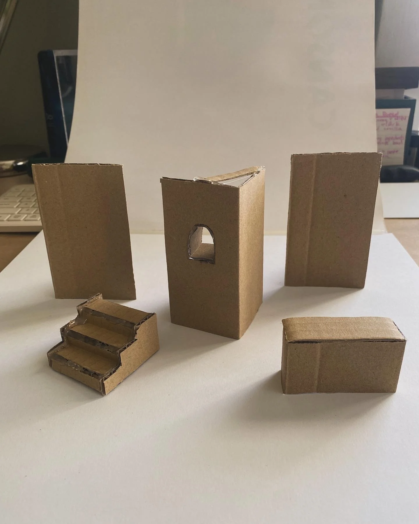 Small cardboard models of stairs, pillars, and a rectangular block placed on a white surface.