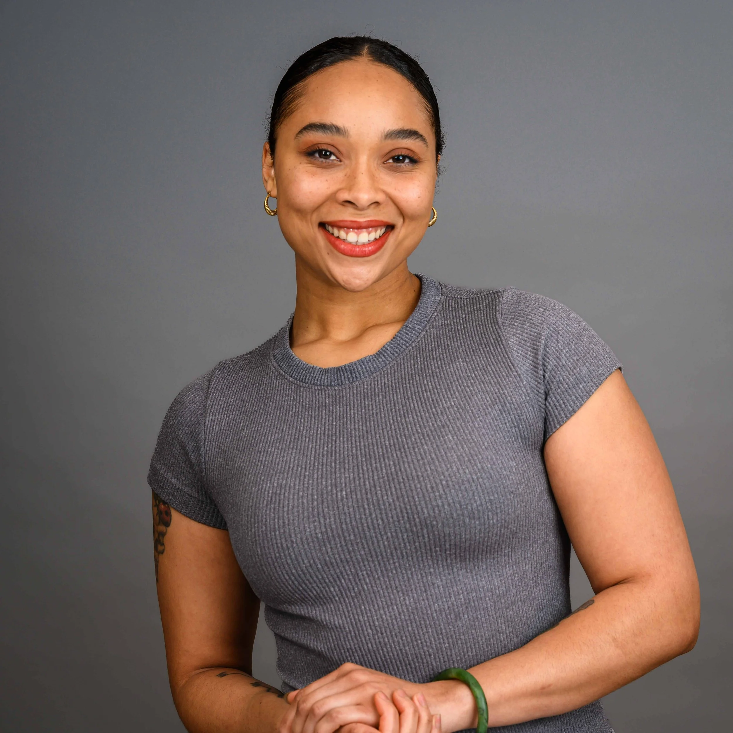 Teacher Jinji, smiling, wearing a gray t-shirt, against a gray background.