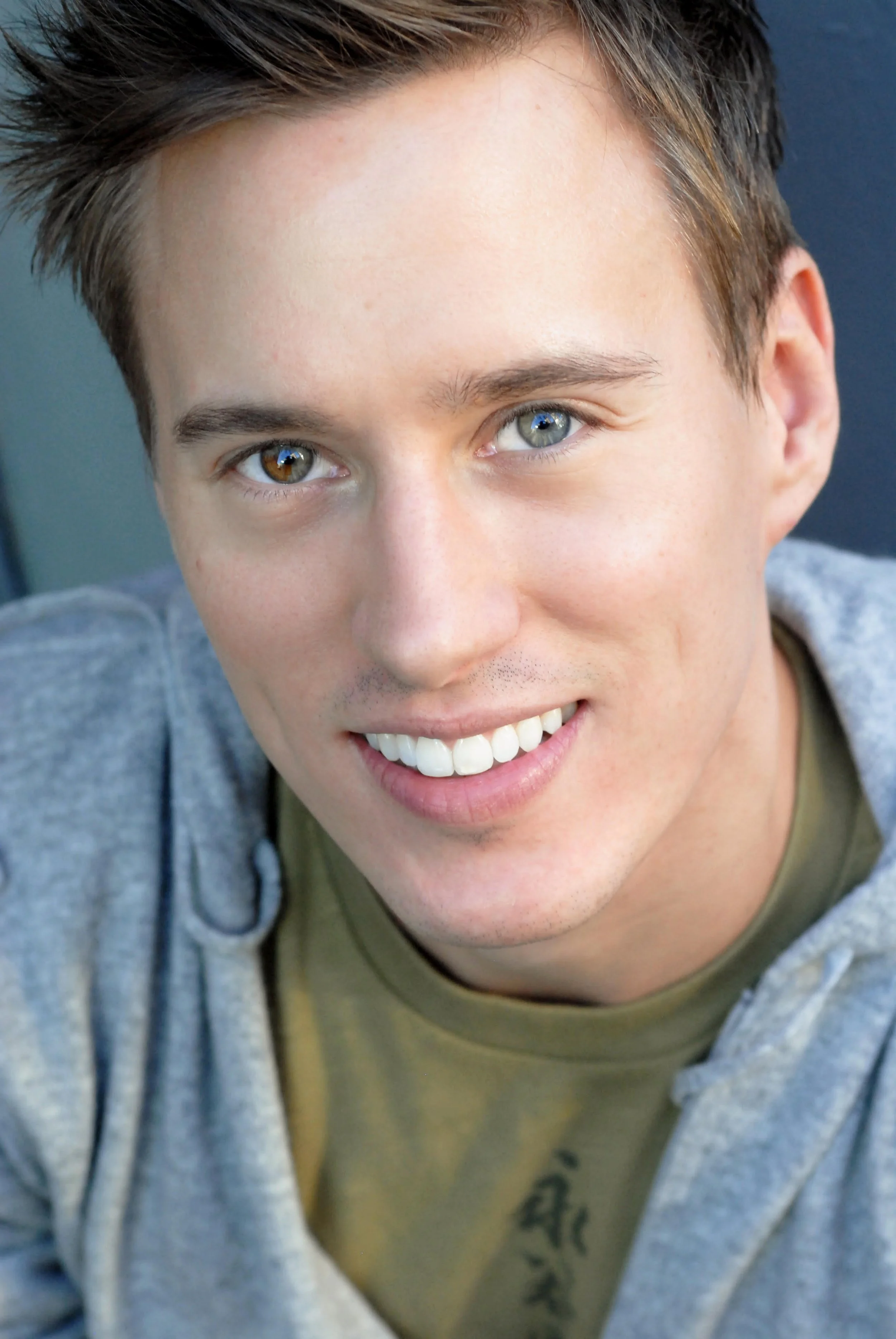 Teacher Kurt, smiling, showing white teeth and blue-green eyes, wearing a grey hoodie.
