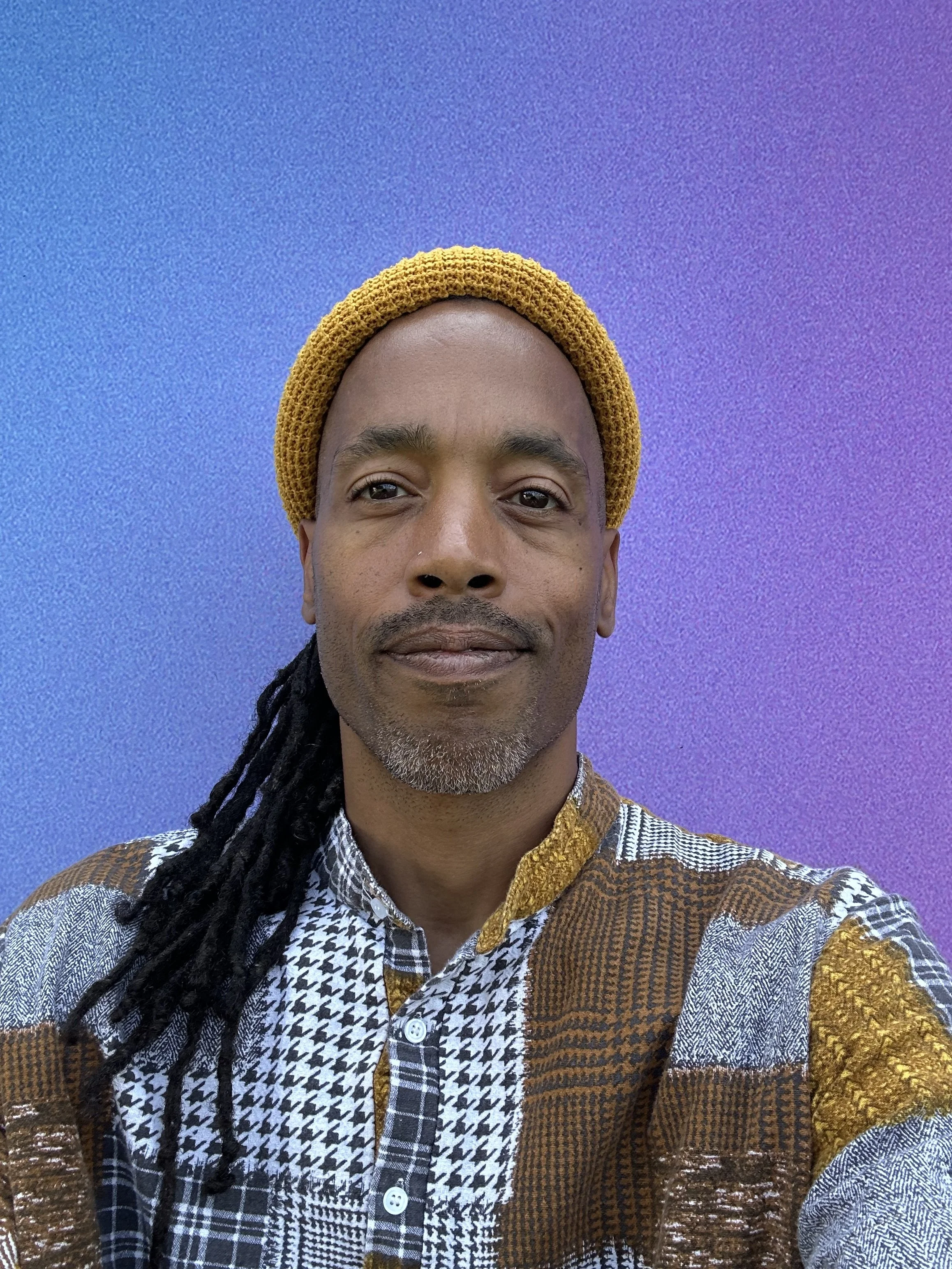 Teacher Orb with a smile, wearing a beanie and a patchwork top.