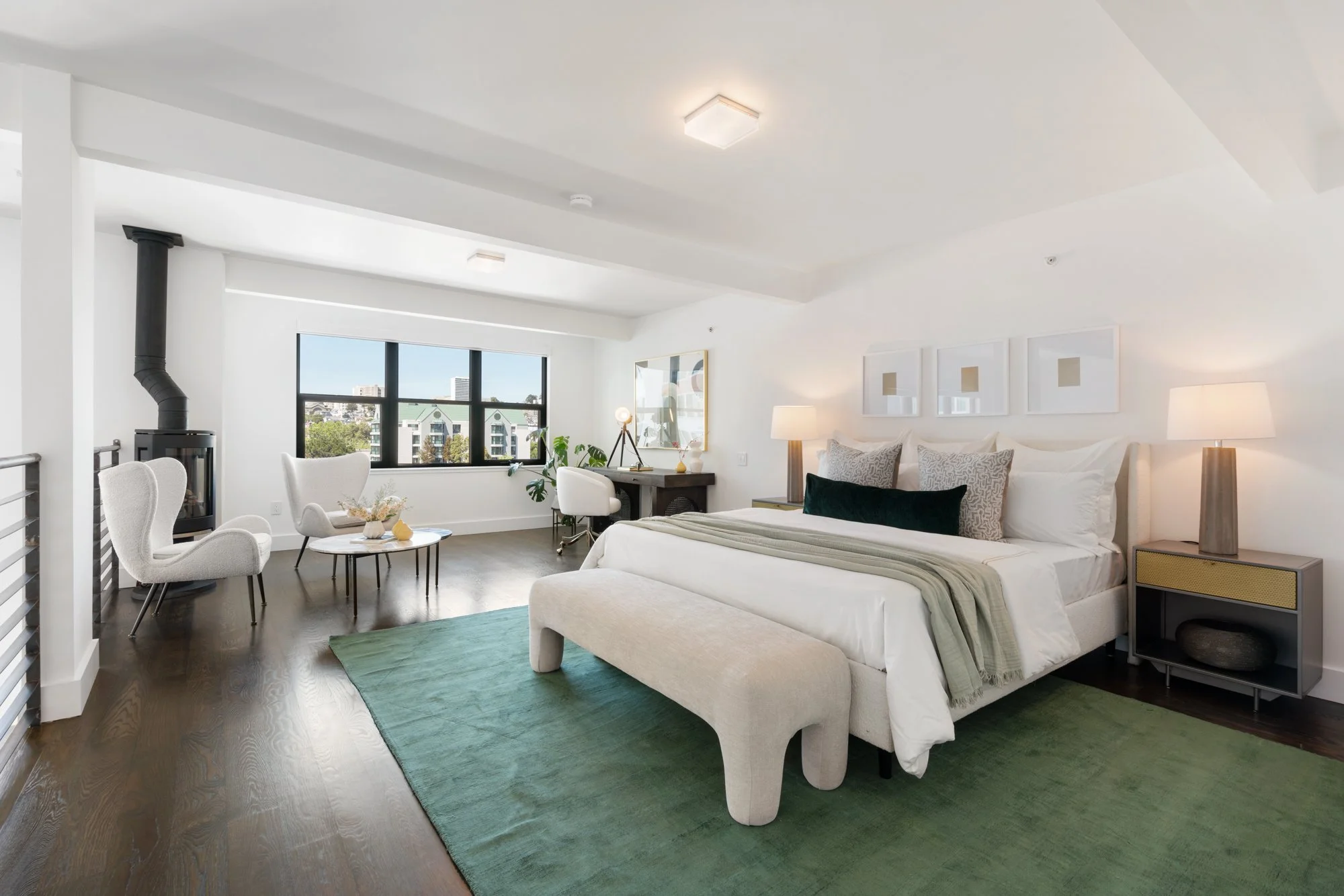 Bright and modern studio apartment with a large bed, armchairs, a small coffee table, a desk with a chair, large window with city view, and contemporary decor.