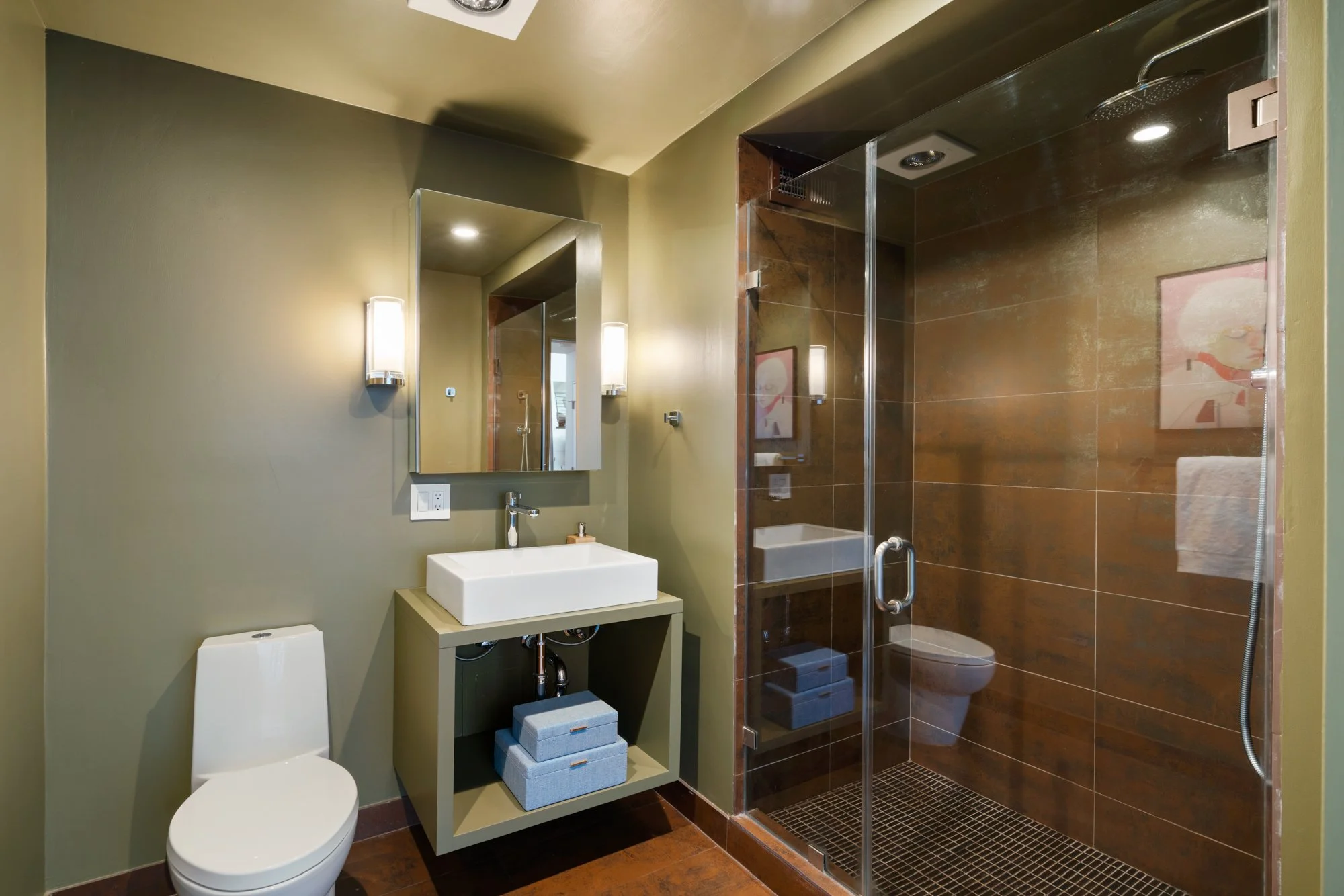 Modern bathroom with green wall, white sink, tall mirror, toilet, and shower with brown tiles, glass door, and rain showerhead.