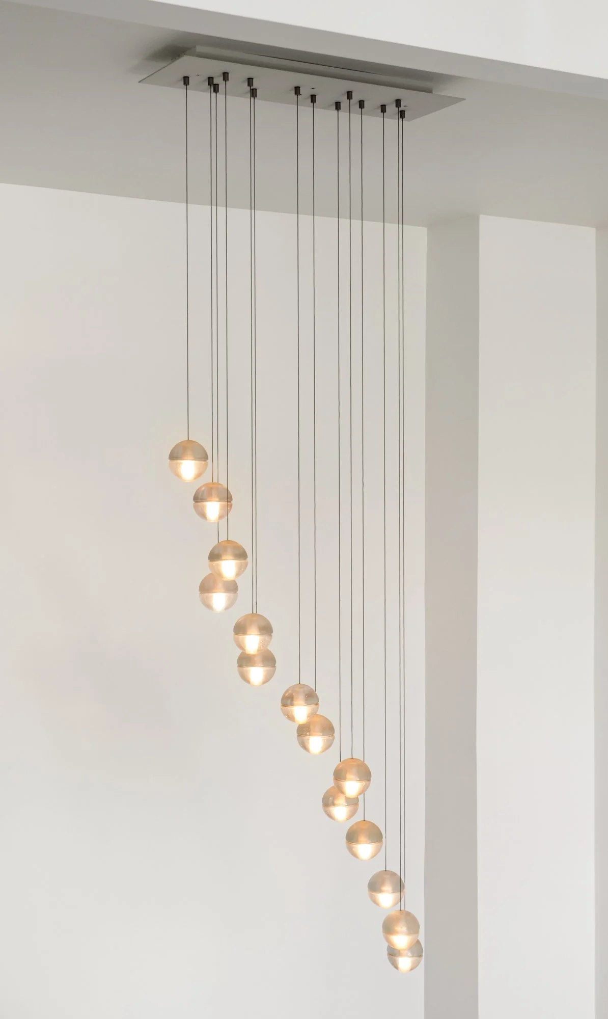 A modern pendant light fixture with multiple spherical lamps hanging at varied lengths from a rectangular ceiling mount in a white interior.