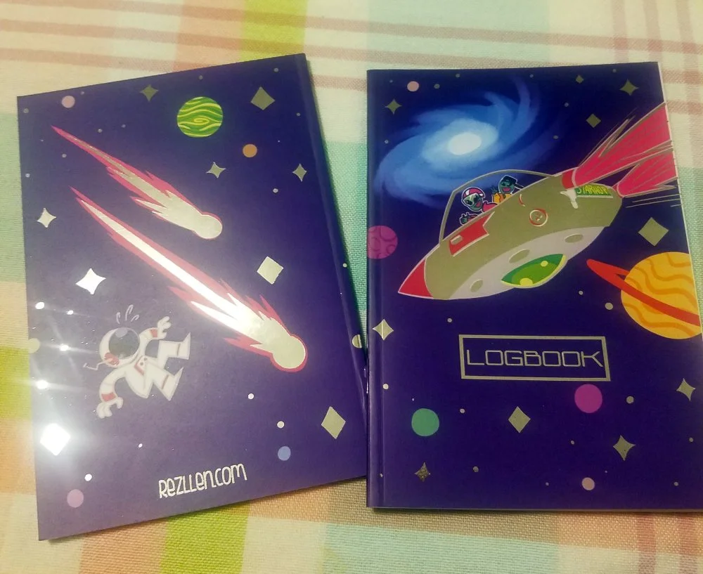 Two science fiction-themed notebooks with space illustrations on a checkered tablecloth.