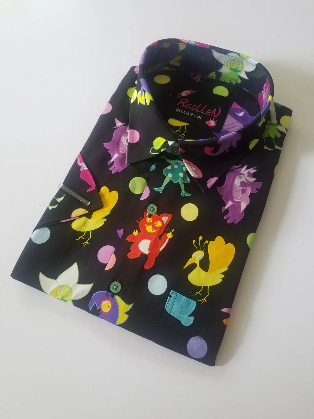 A folded black button-up shirt with colorful cartoon chicken characters and polka dots, laid on a white surface.