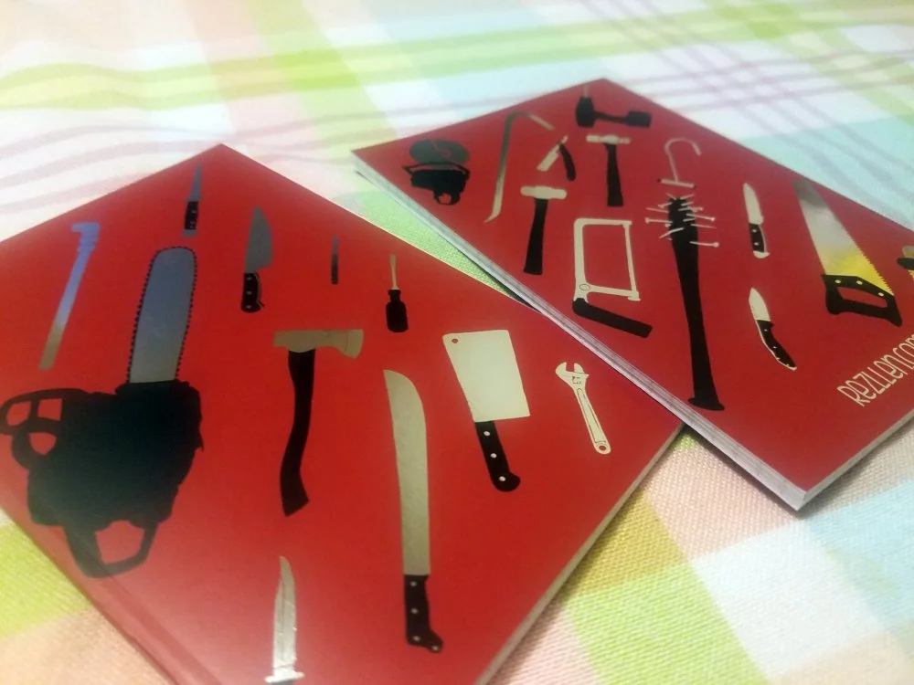 Two red cards with black and white illustrations of various tools such as a chainsaw, screwdriver, wrench, saw, and knives, on a checkered cloth background.