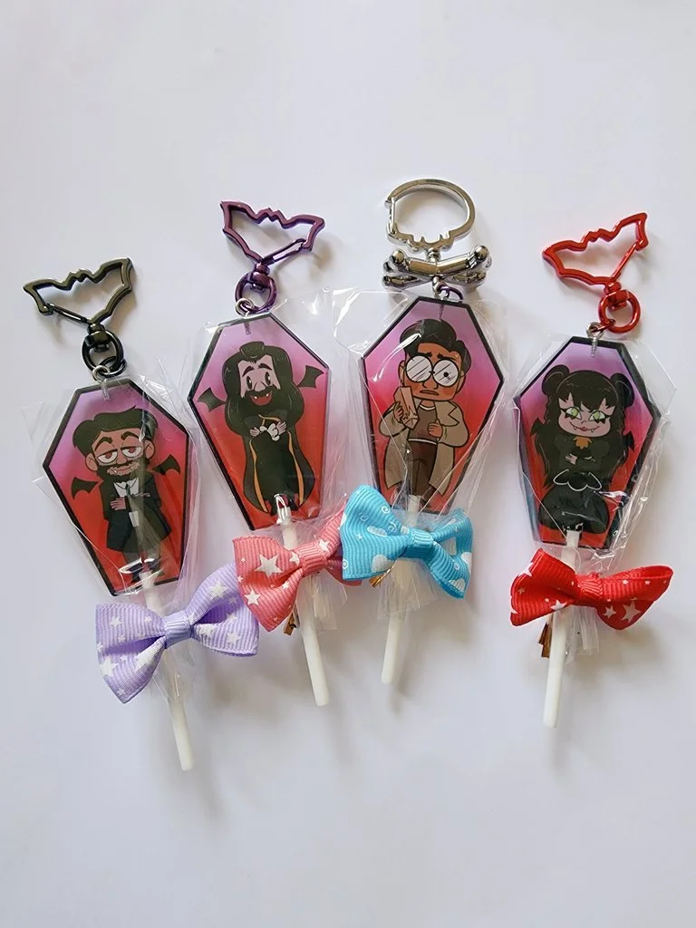 Four cartoon character keychains with matching bows and lollipops, each featuring a different character with distinct clothing and hairstyles, attached to colorful clip hooks.